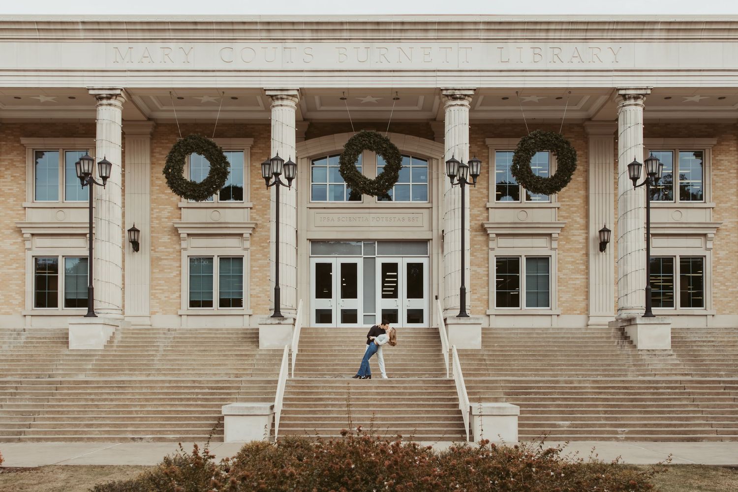Three large evergreen wreaths hang above the entrance of a grand stone building with symmetrical staircases. Wedding photographer DFW