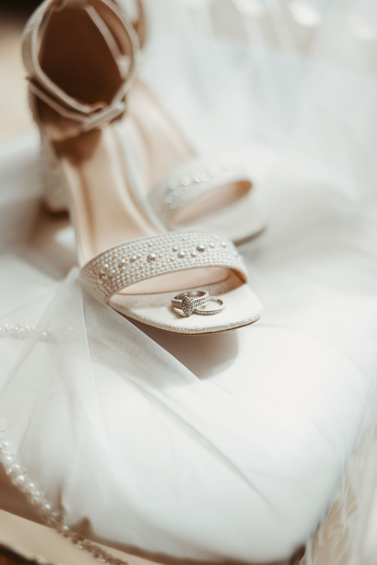 Wedding rings rest delicately on an elegant white bridal shoe with crystal embellishments. Wedding photographer DFW