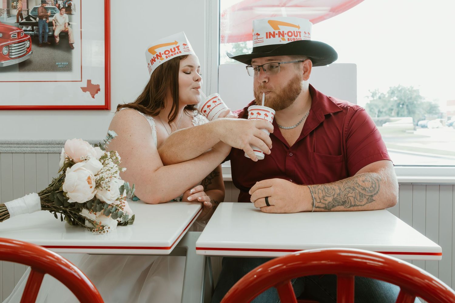 A couple shares milkshakes at a retro-style diner table with flowers.