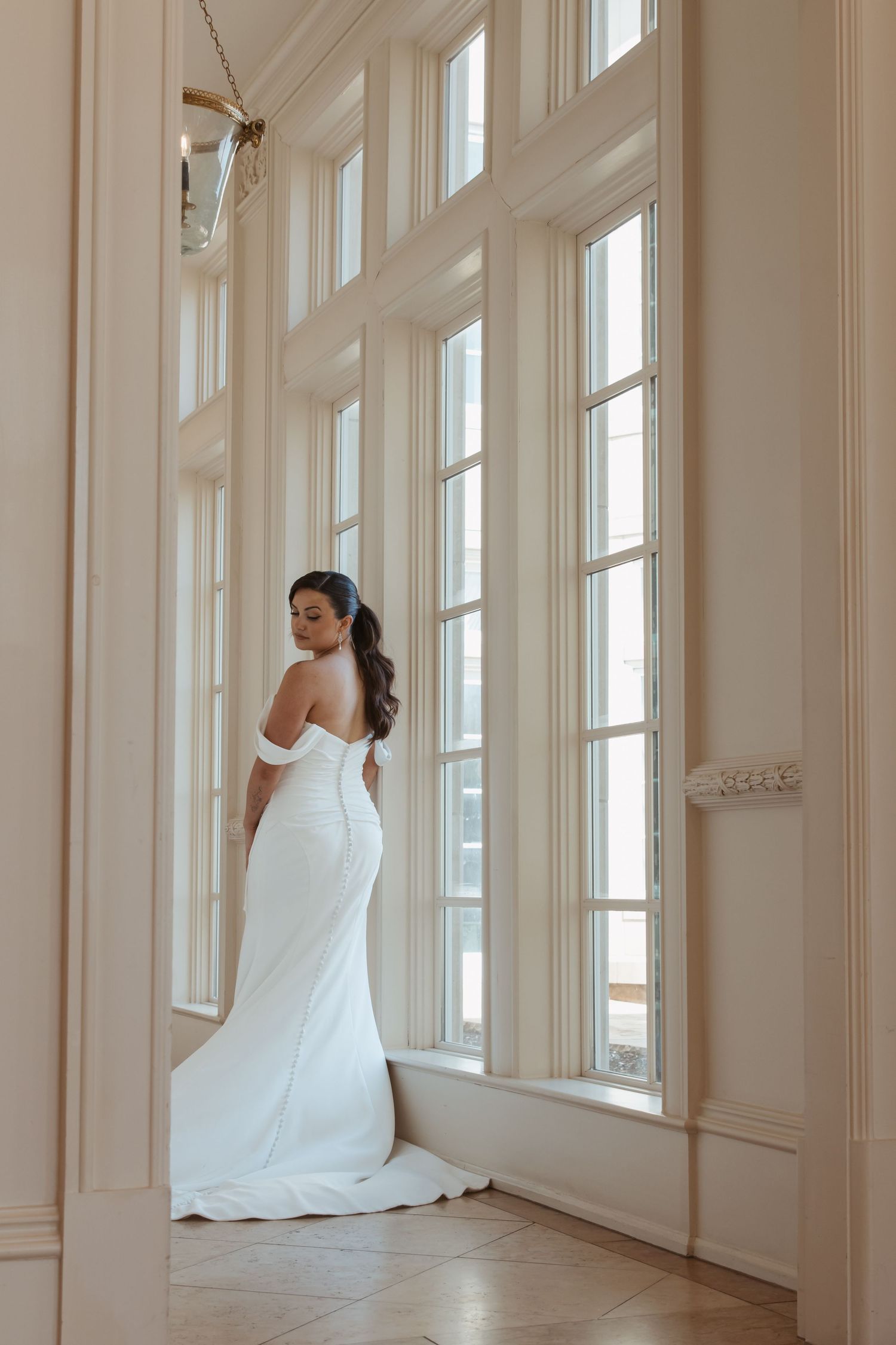 Ethereal bridal portraits captured in a sunlit corridor with tall windows and white walls.