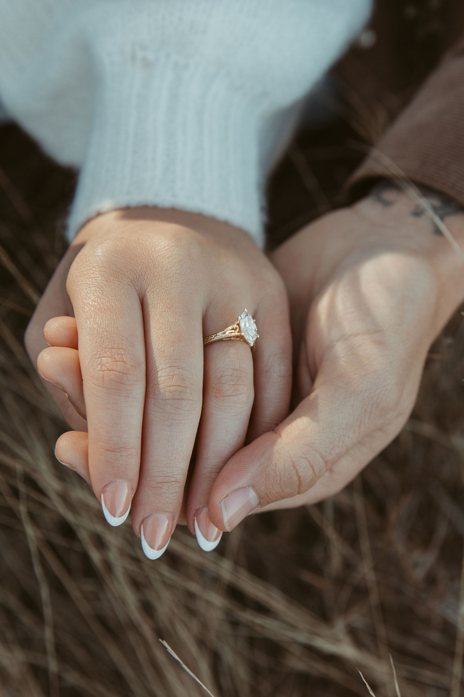 A delicate diamond engagement ring sparkles on a hand resting against a dark textured background. engagement photos DFW