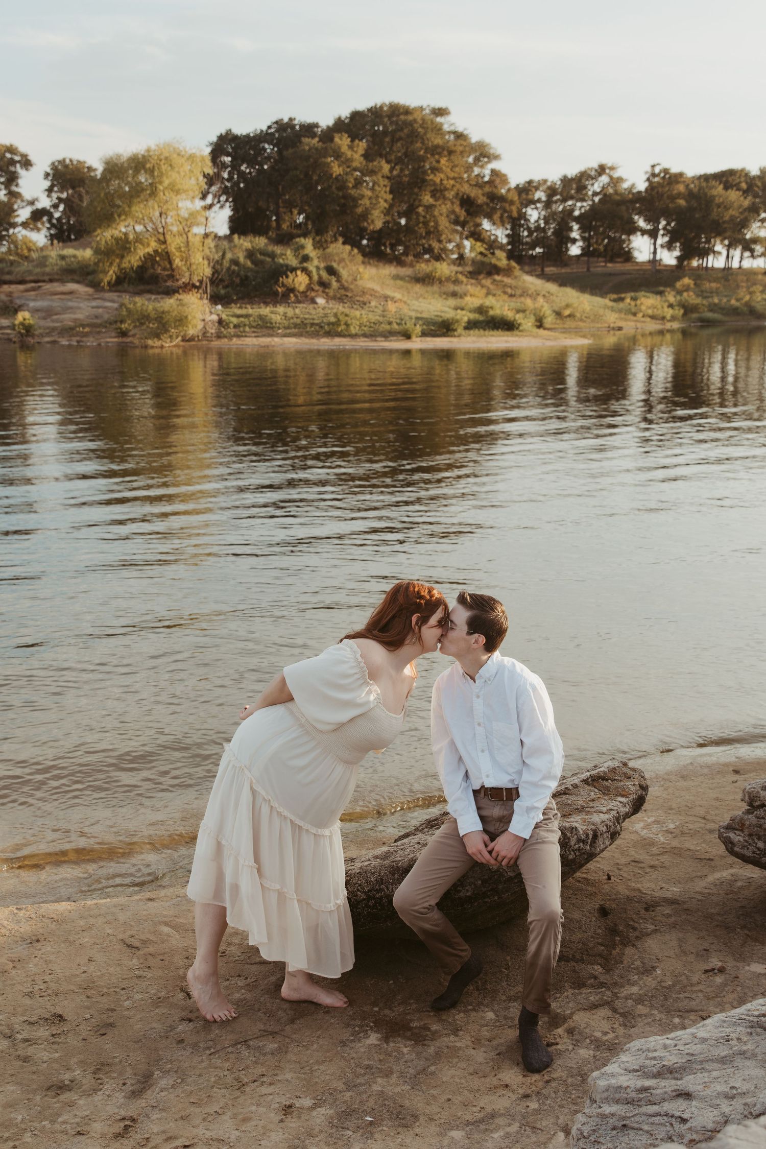 Couple sharing intimate moment on rocky shoreline during golden sunset.