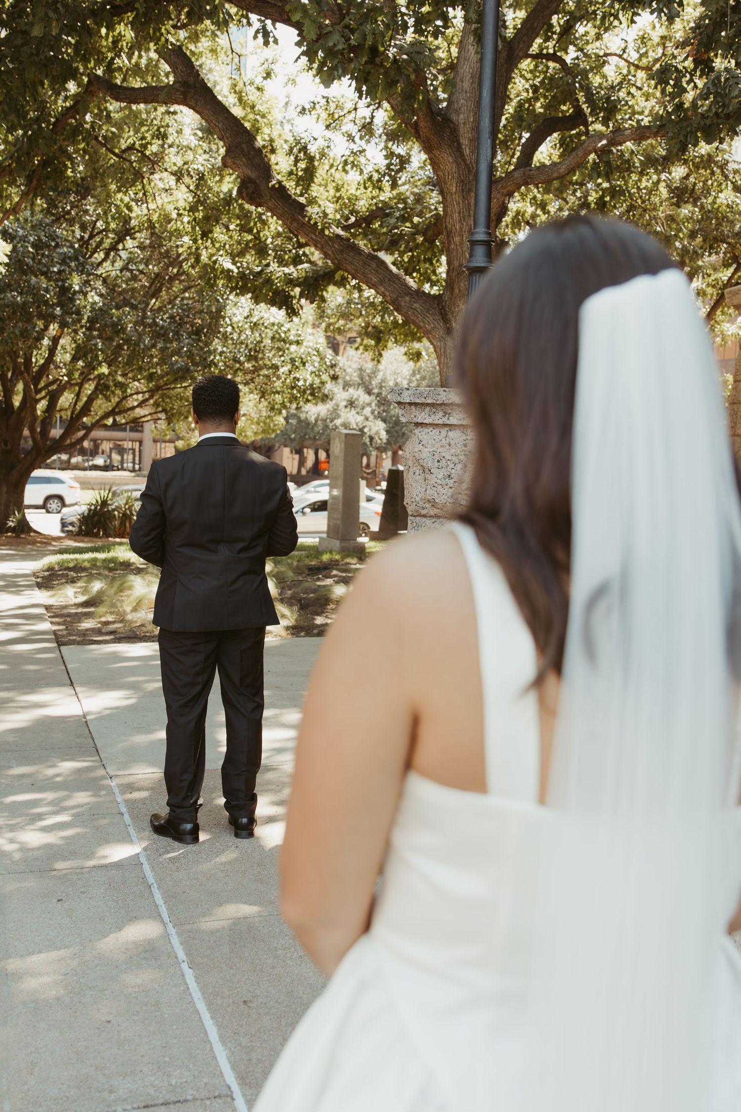 A couple walking together outdoors on a sunny day, captured from behind. Wedding Photographer DFW