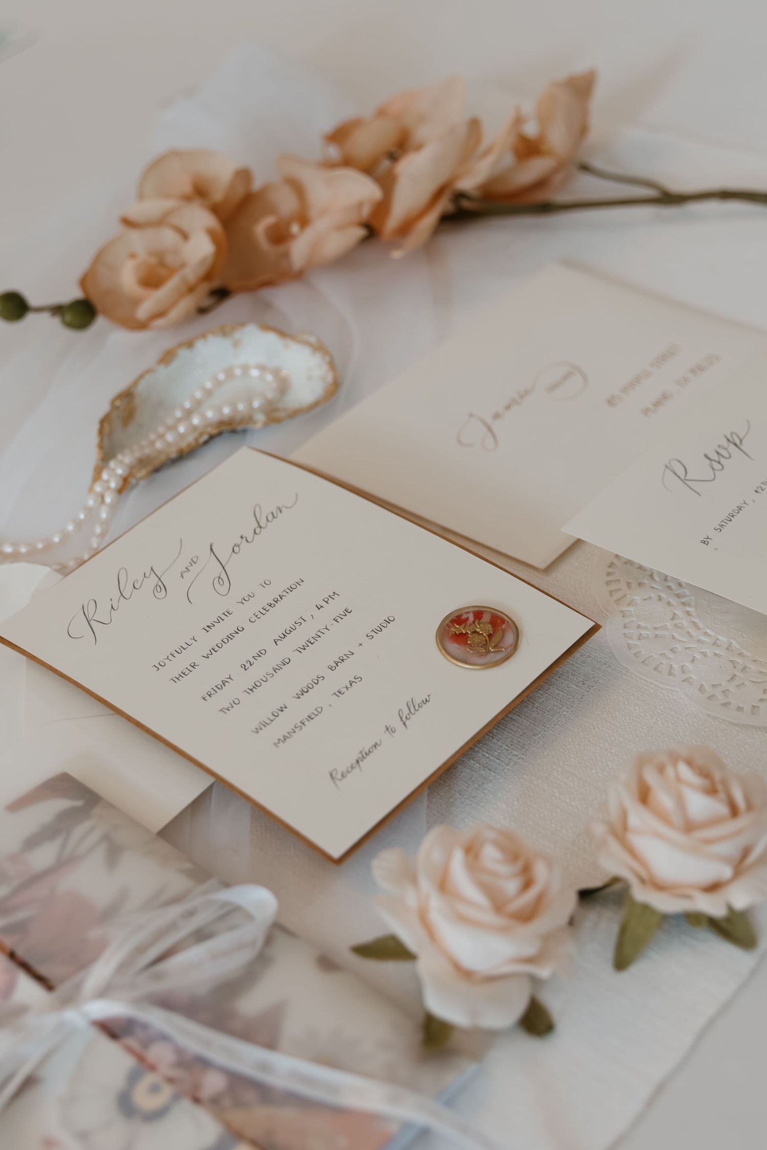 Elegant wedding invitations with blush roses and pearl details arranged on a light neutral surface.