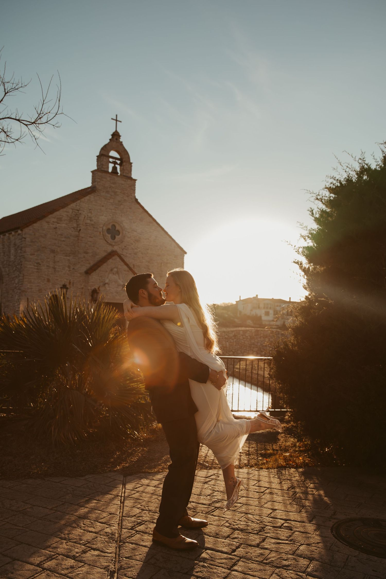 A romantic sunset silhouette scene with a church bell tower in the background on a cobblestone path.