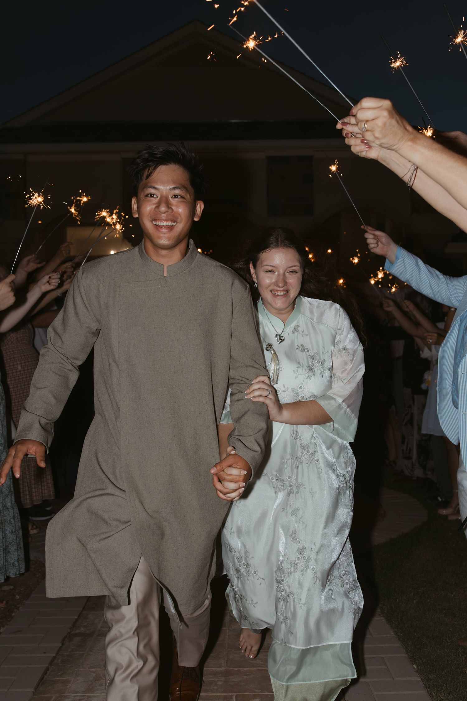 A couple runs joyfully while holding sparklers during an evening outdoor celebration.