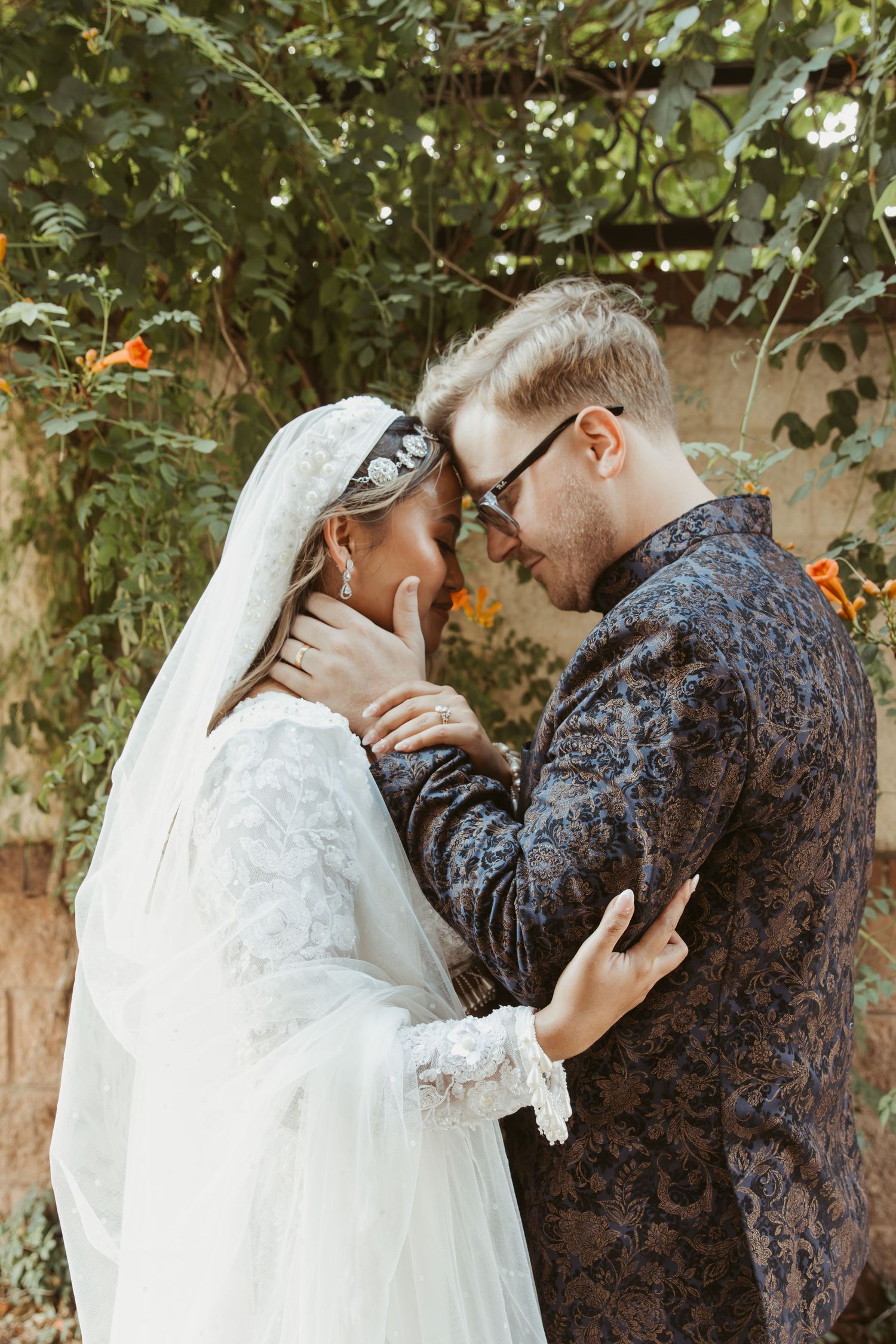 A couple in wedding attire share an intimate moment against a backdrop of greenery and autumn colors.