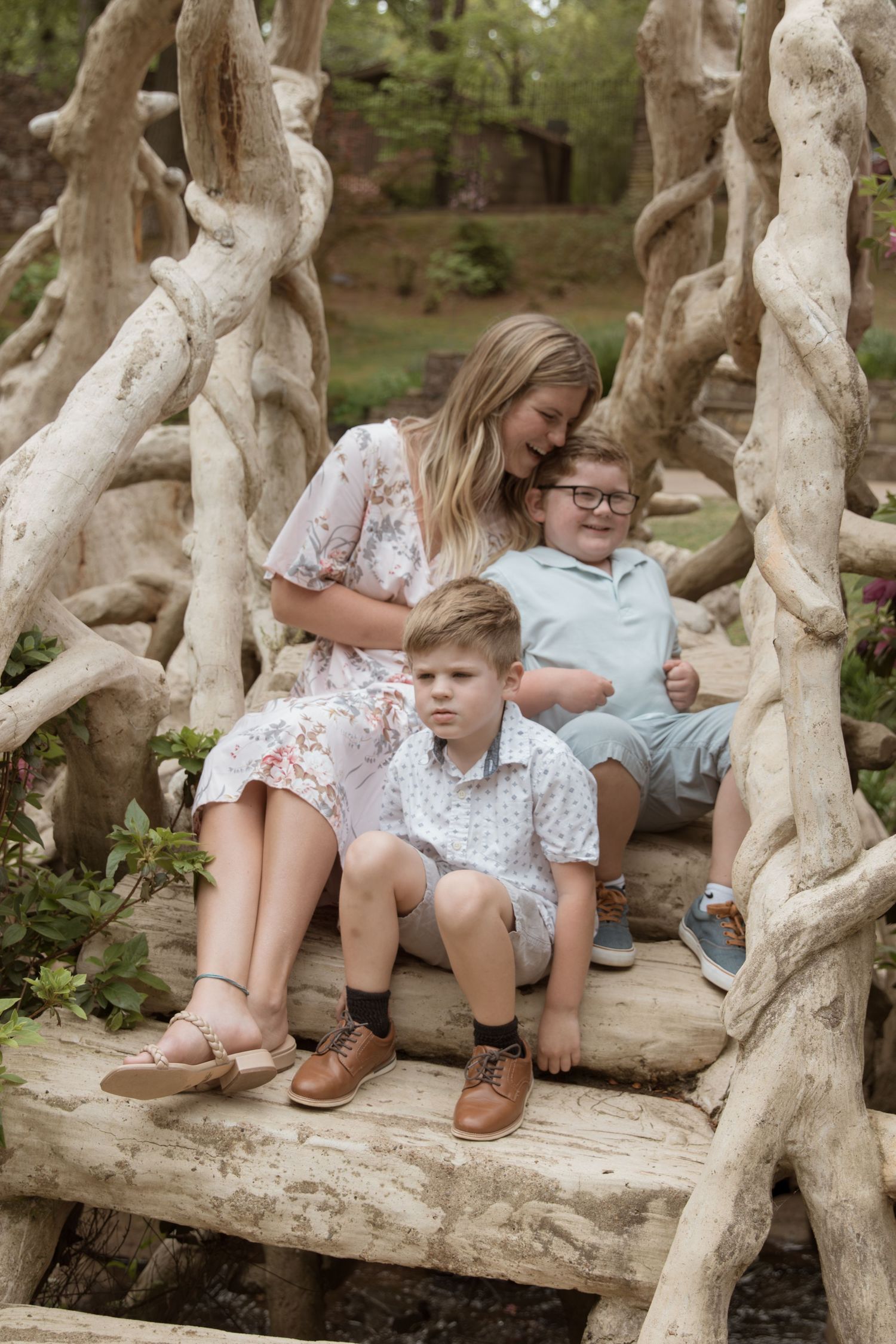 People sit together on rustic wooden steps surrounded by twisted tree branches in a forest setting.