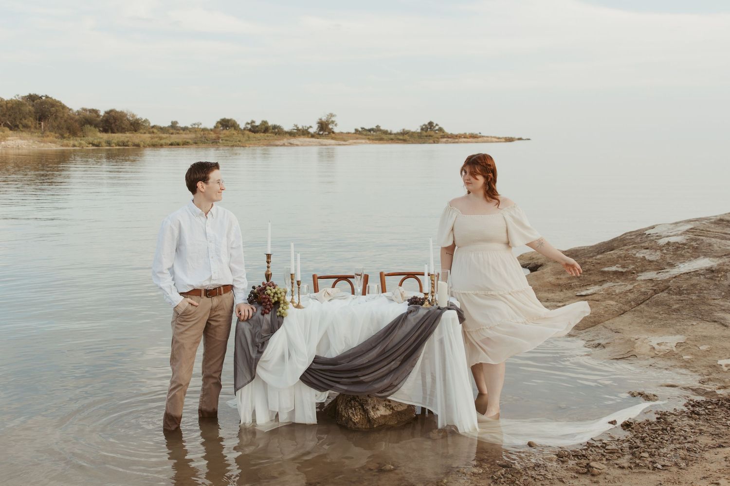 Couple having romantic picnic setup on rocky shore with blanket and decorations.