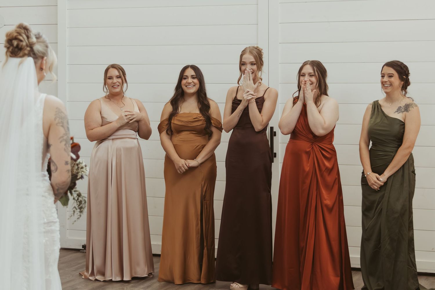 Group wearing coordinated earth-toned dresses in rust, brown, and olive green colors stand together in a row. Wedding Photographer DFW