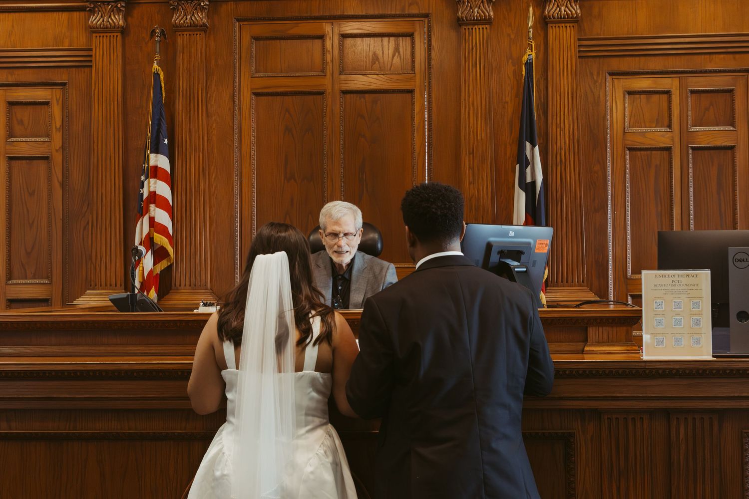 A courthouse wedding ceremony with American flag and wooden judicial furnishings in the background. Wedding Photographer DFW