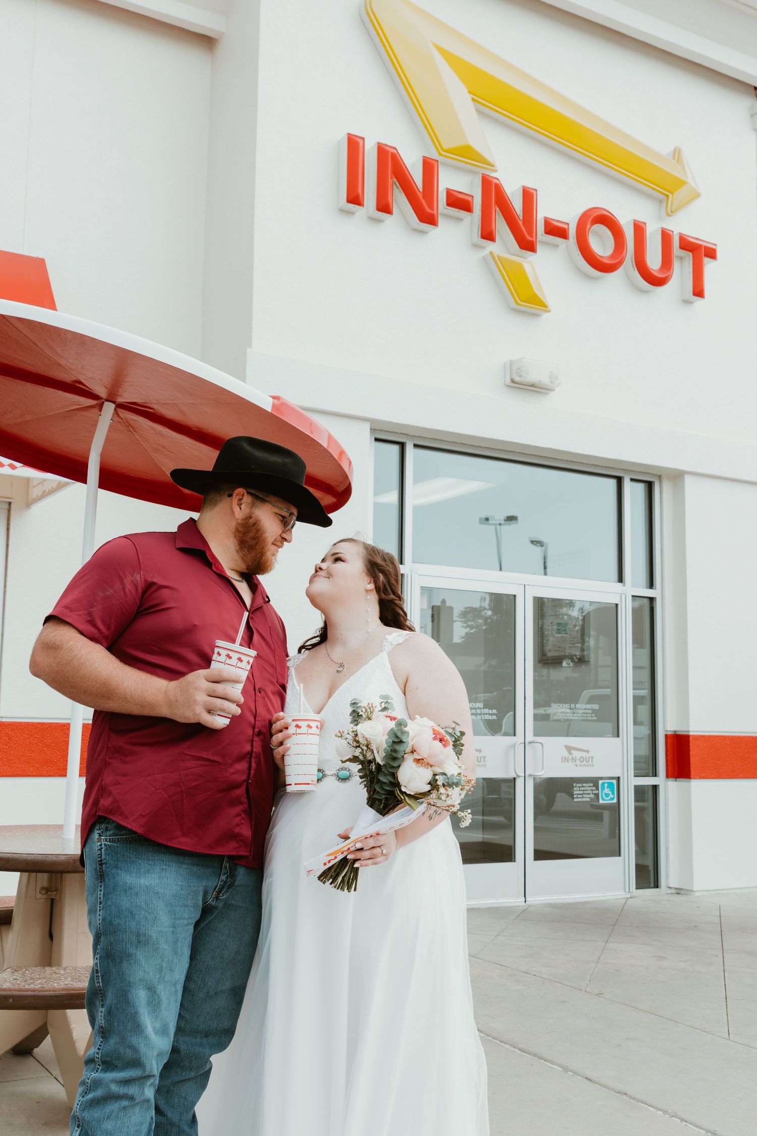 Newlyweds share drinks outside an In-N-Out Burger restaurant entrance.