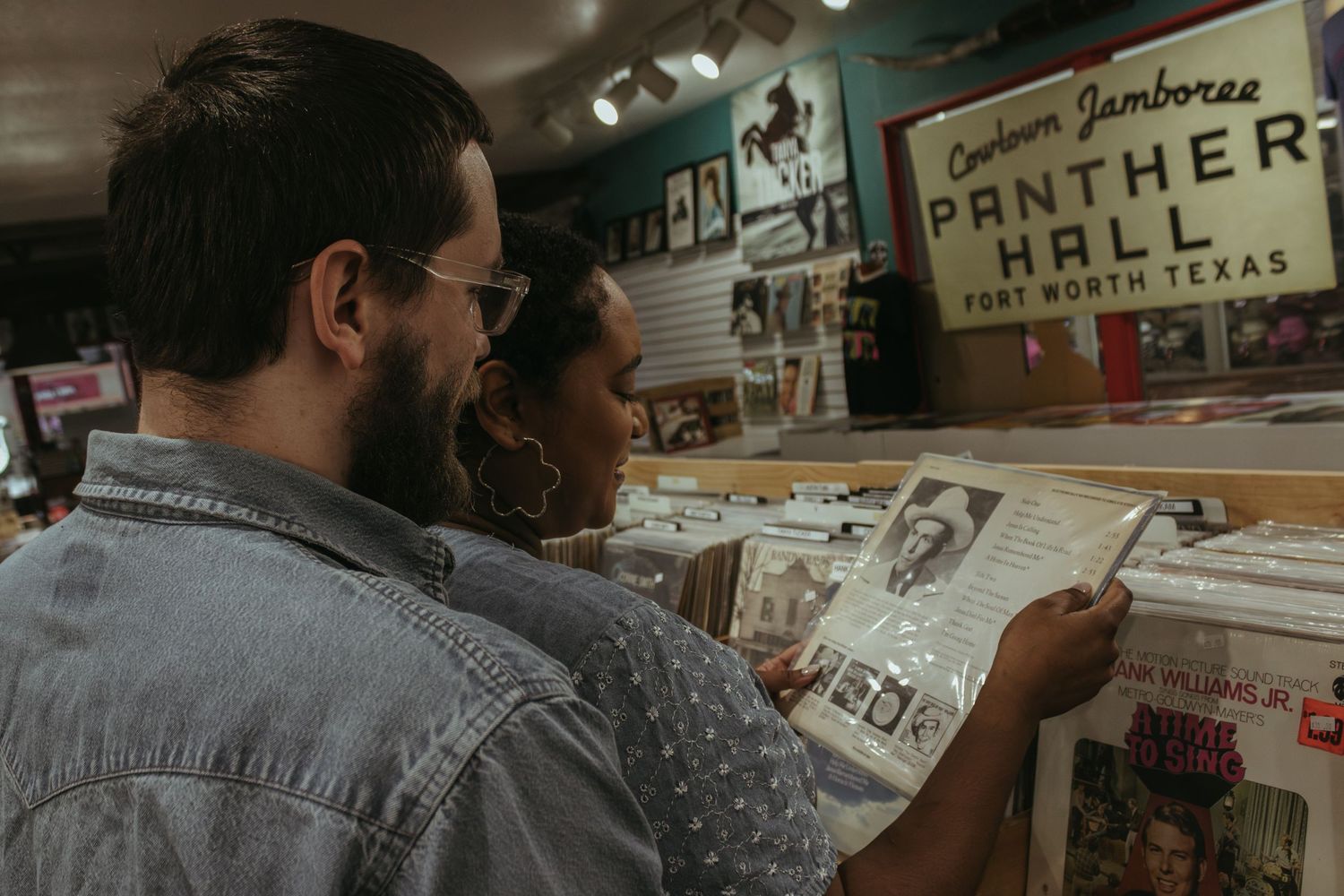 Two people browse through vinyl records at a vintage record store with retro signage on the wall.