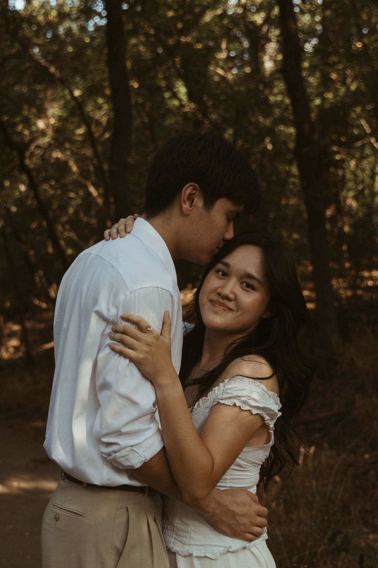 Couple embraces in a romantic golden hour photoshoot among trees in a natural outdoor setting.