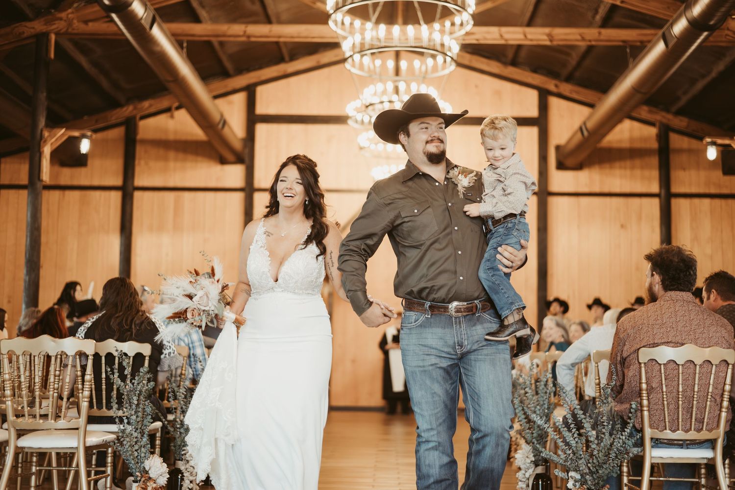 Wedding reception guests dancing together in a rustic wooden barn venue with warm lighting and elegant decor.
