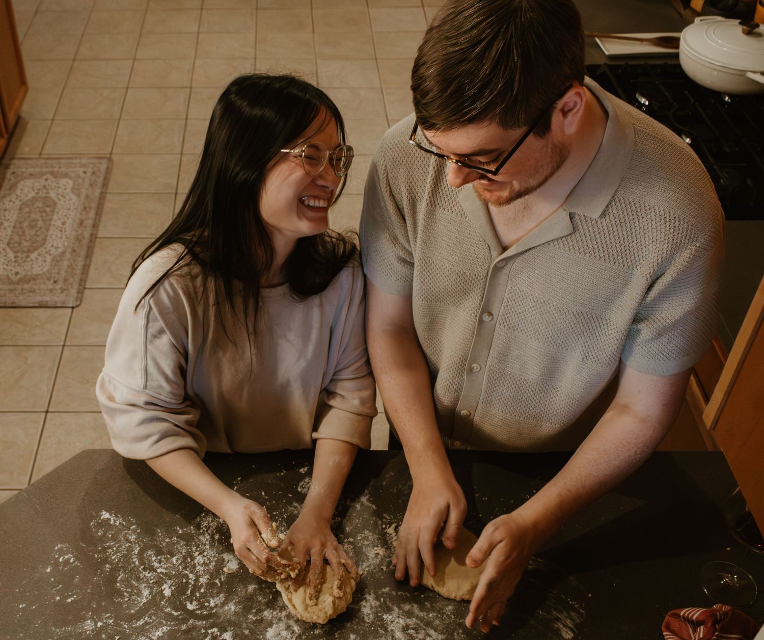 A couple kneads dough together on a flour-dusted countertop.