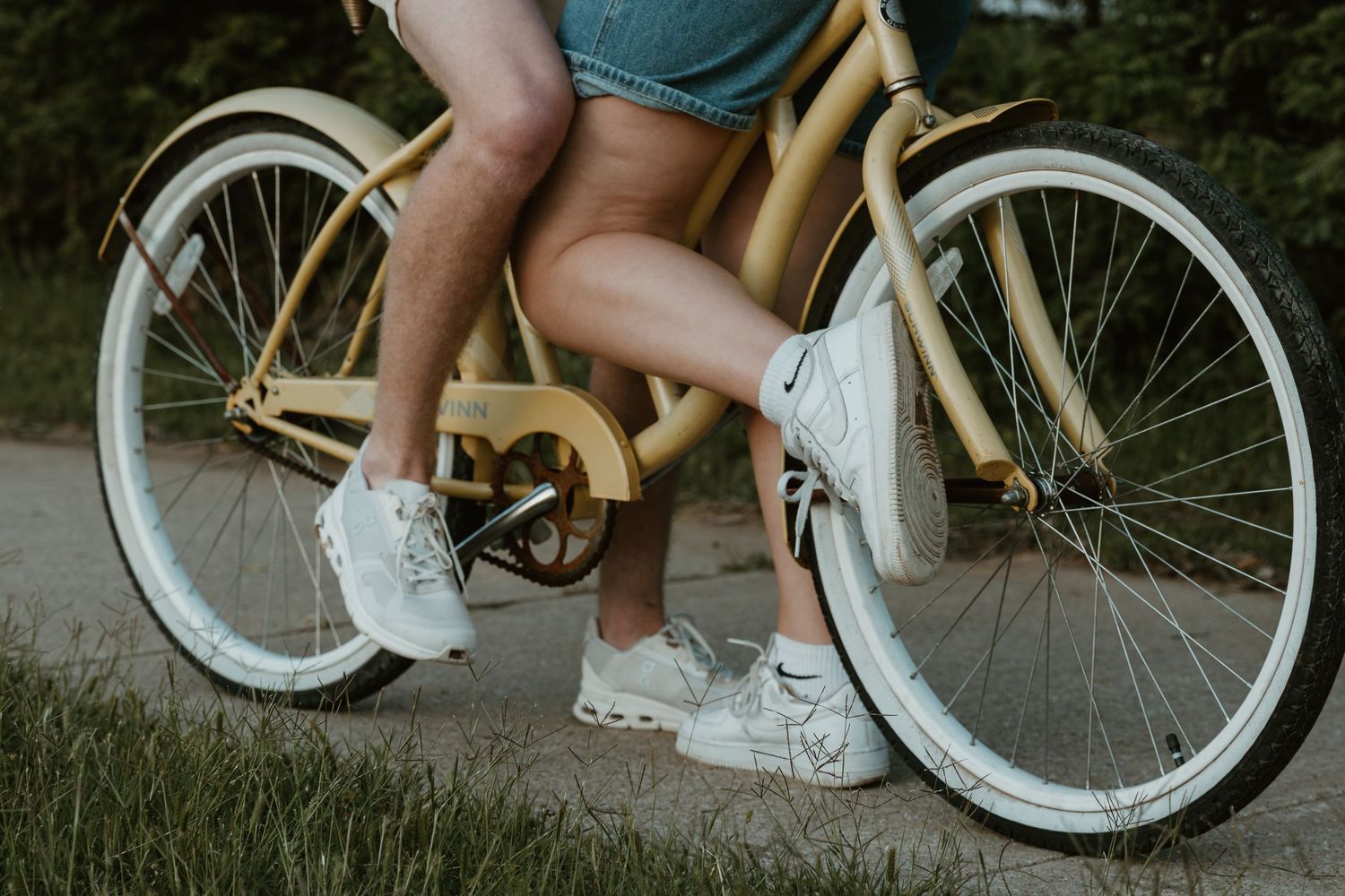 Vintage style cream-colored bicycle with white tires and white sneakers pedaling down a path at dusk.