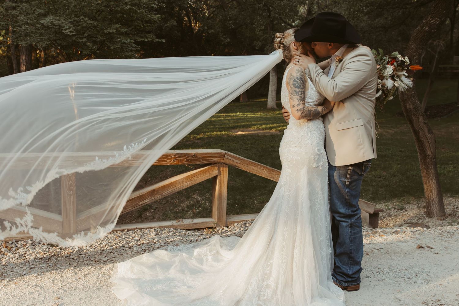 A flowing wedding veil catches the breeze as a couple embraces in a romantic outdoor setting. Wedding Photographer DFW