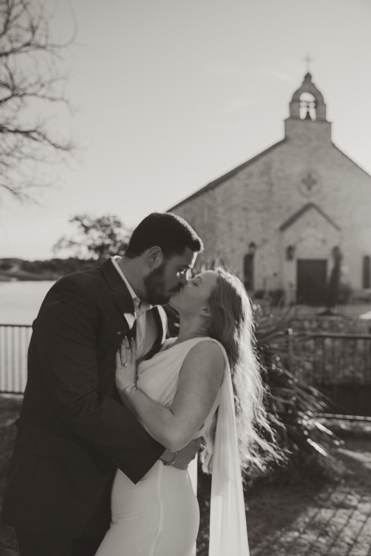 Romantic wedding couple sharing intimate kisses outside a rustic stone church in black and white.