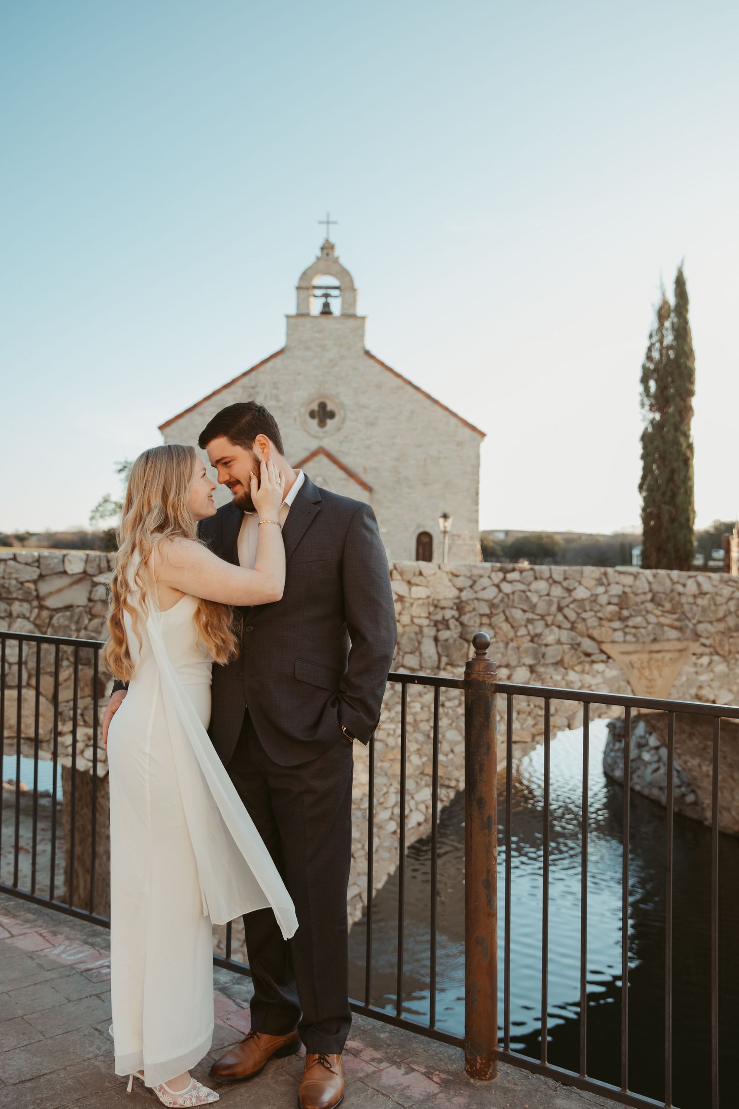 Bride and groom share tender moments along a stone railing with chapel in background.