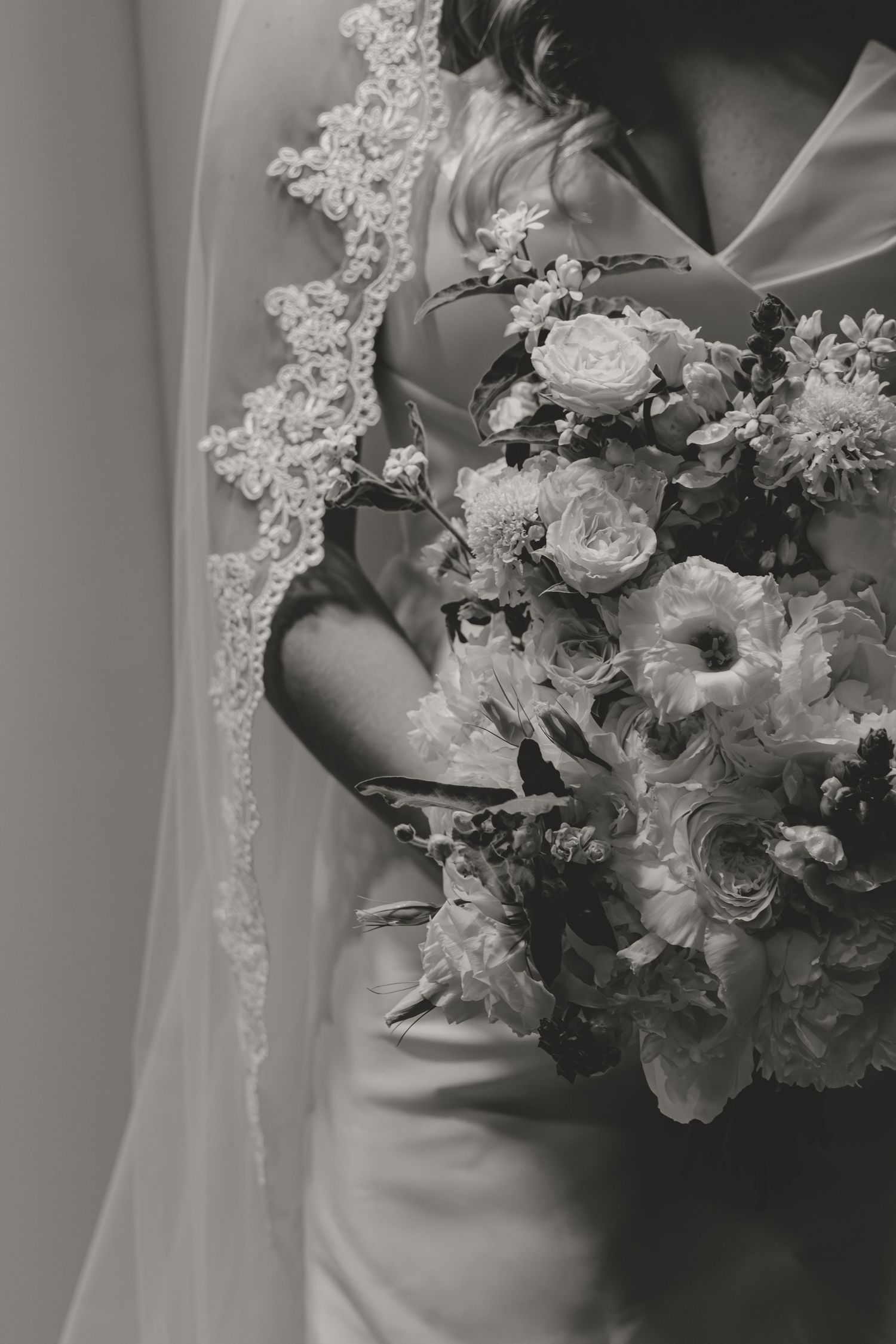 Black and white wedding photo showing lace veil detail and elegant bridal bouquet with roses and mixed flowers.