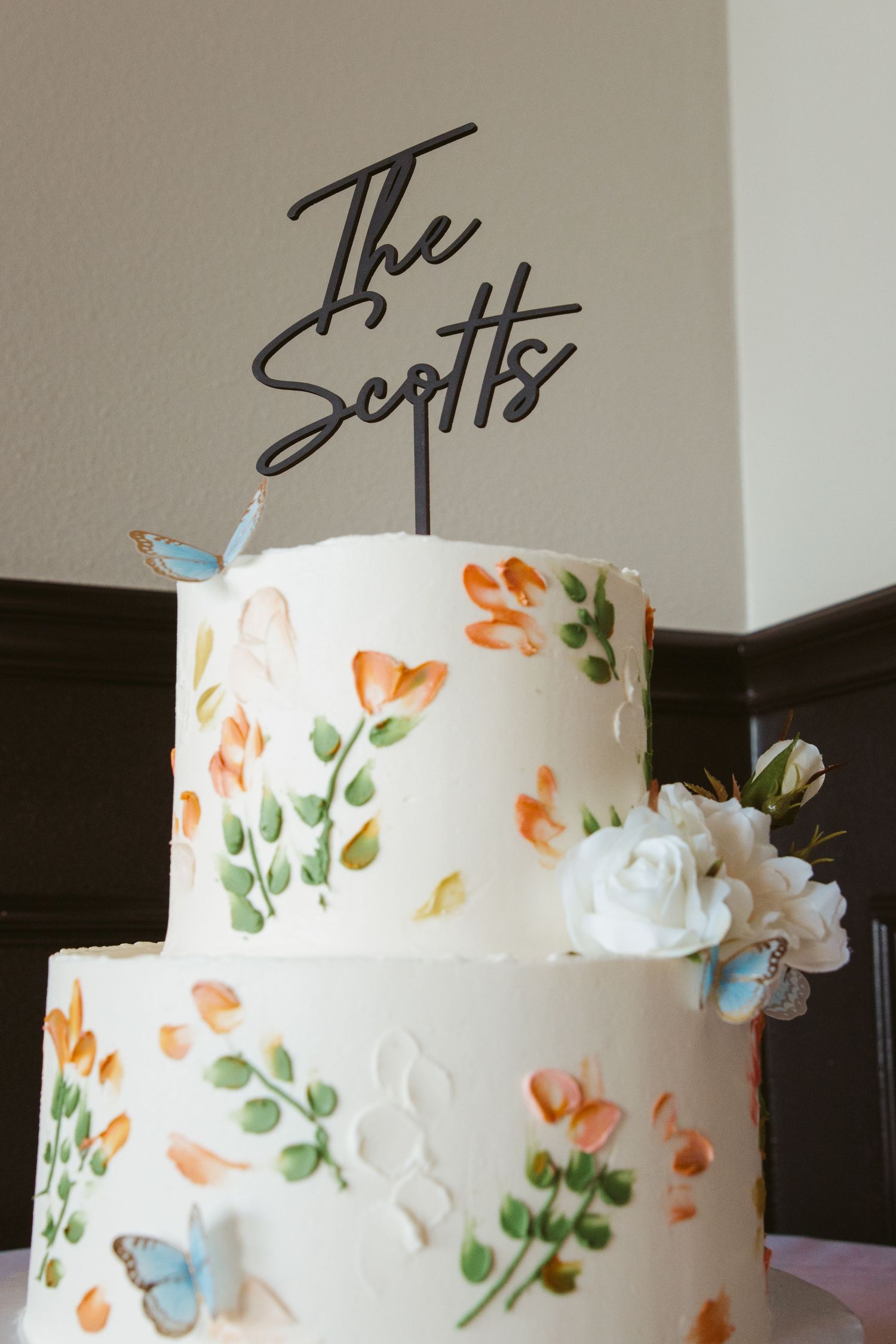 Three-tiered white wedding cake decorated with delicate hand-painted floral designs and butterflies.