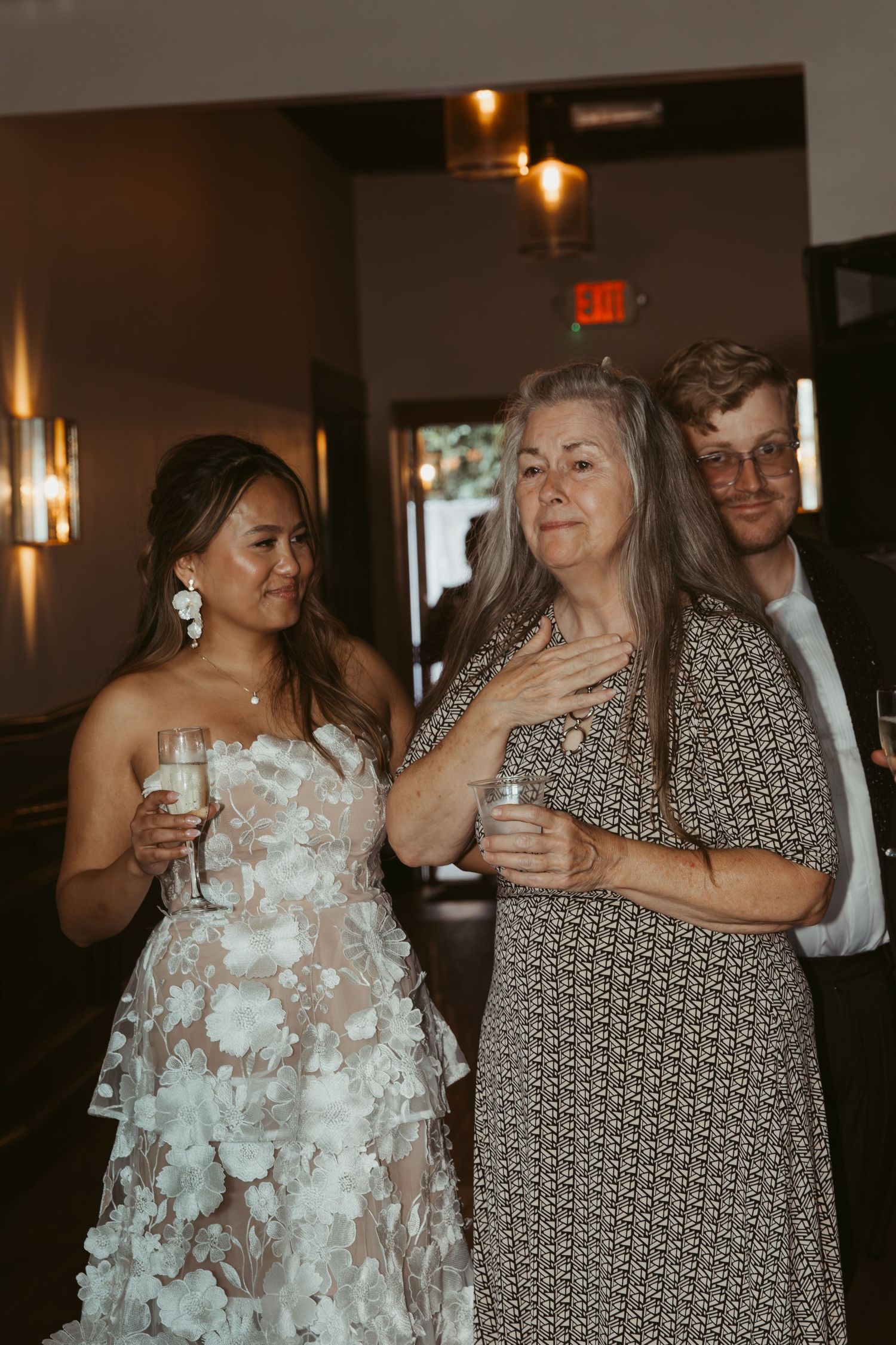 Wedding reception guests celebrate with drinks and laughter in a warmly lit indoor venue.
