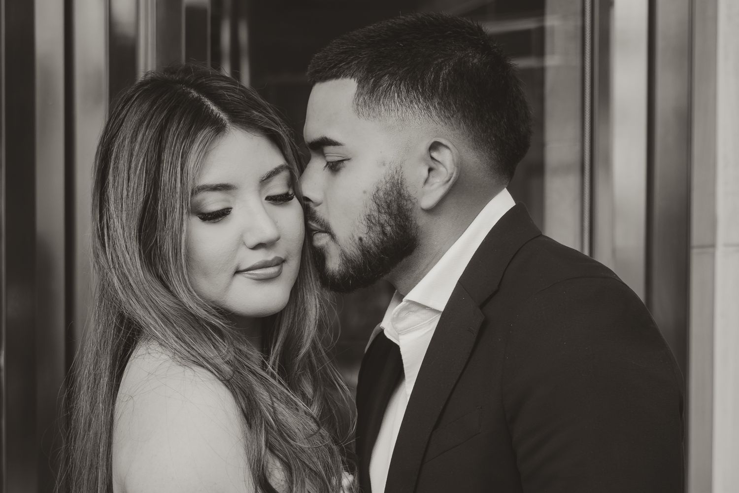 A couple shares an intimate moment in black and white, with her hand gently placed on his bearded face. Engagement photographer DFW