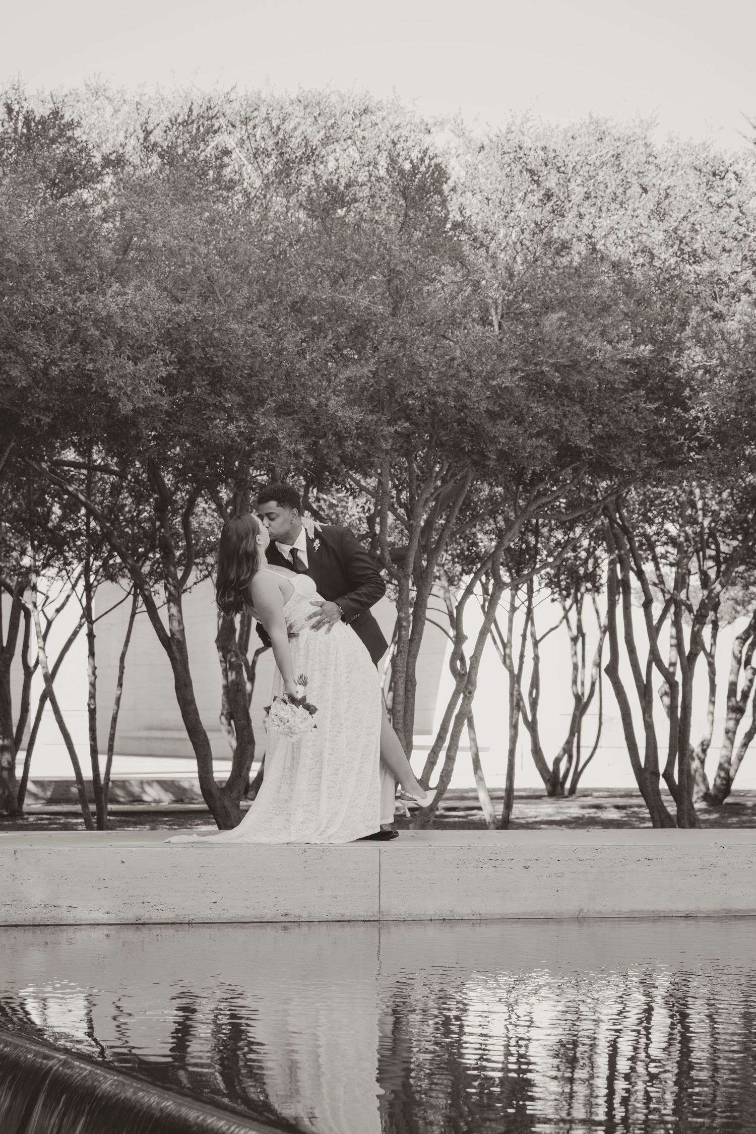 A row of trees reflects on still water creating a serene mirror image along a waterfront. Wedding Photographer DFW