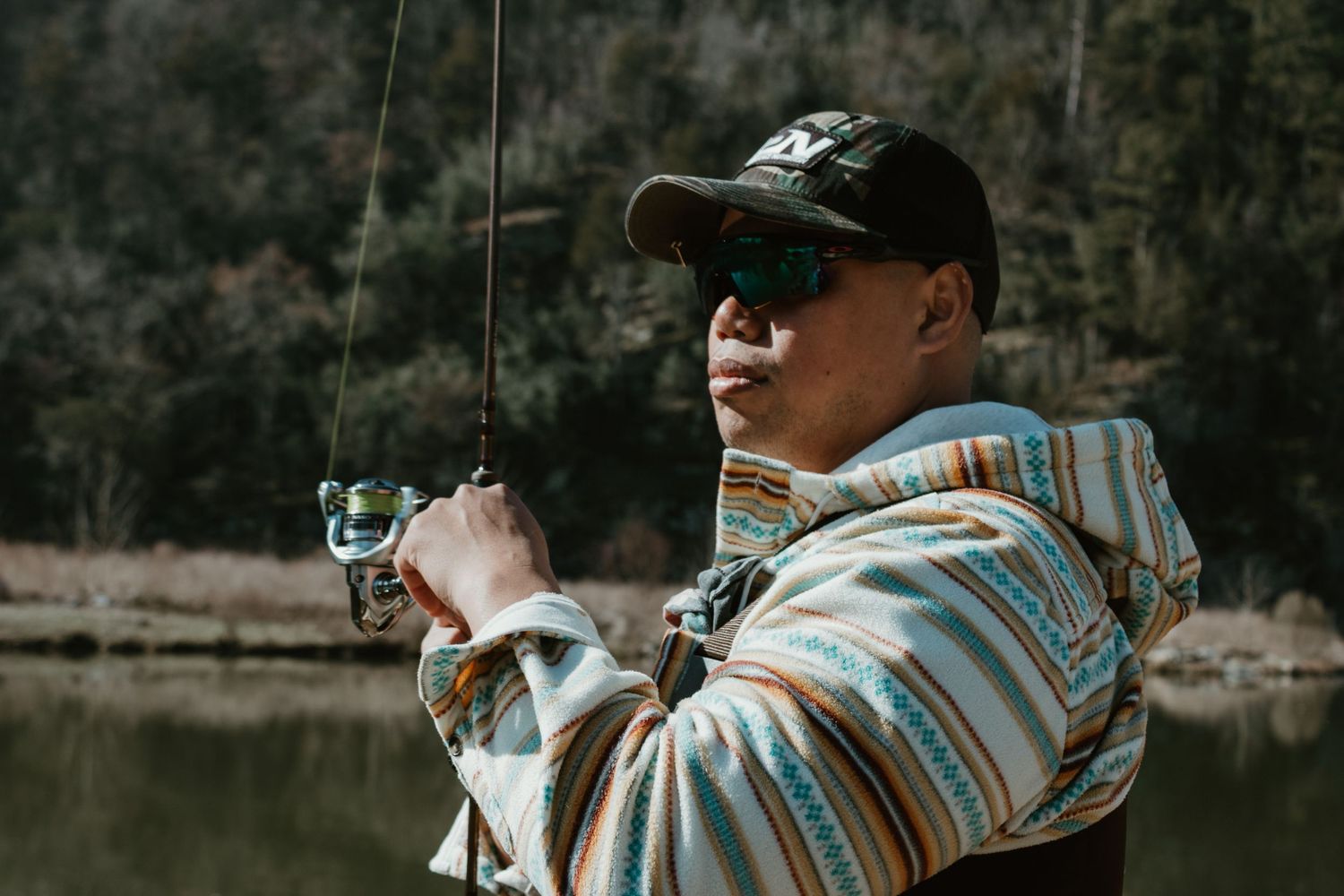 An angler in a striped hoodie casts a fishing line into a river.