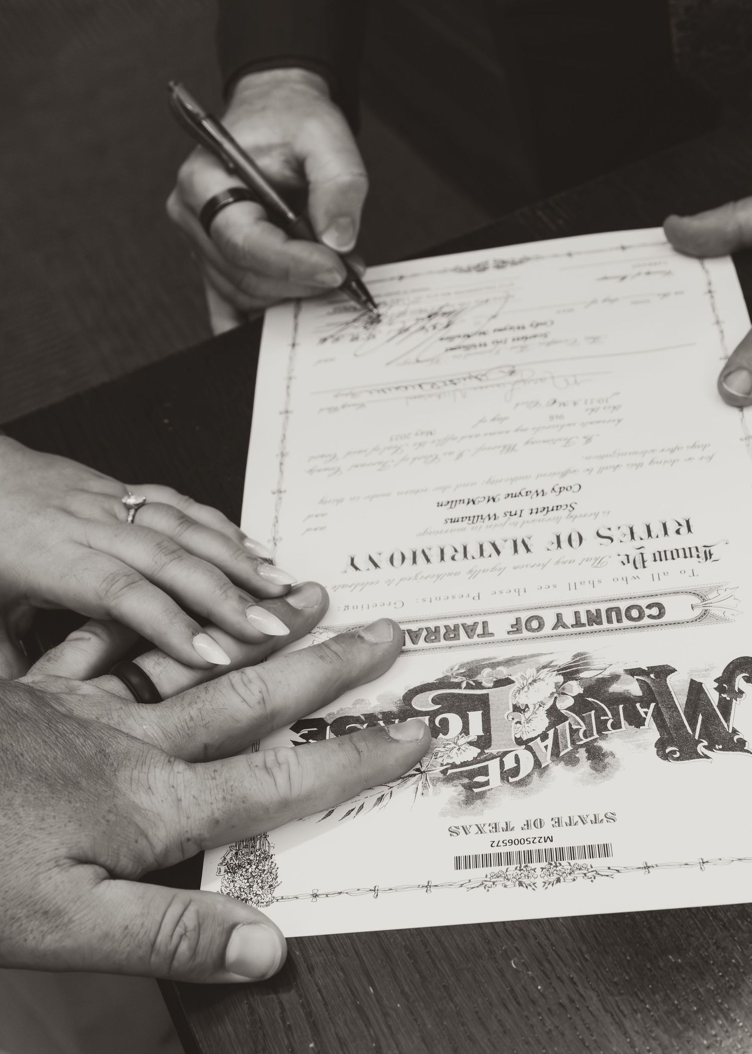 Close-up of hands signing a marriage certificate with wedding rings visible.