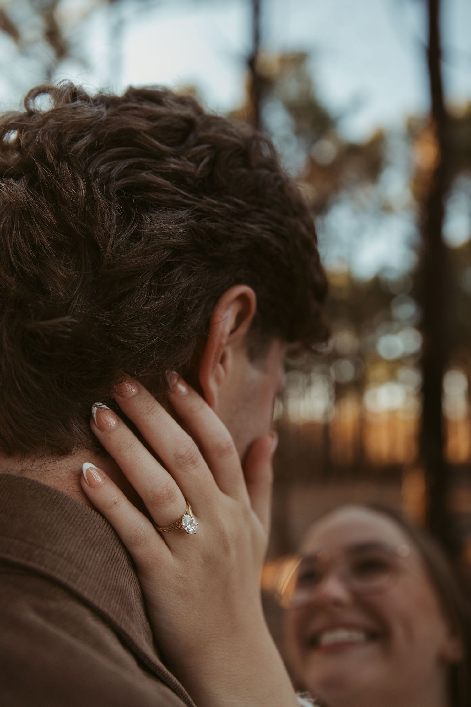 A romantic engagement photo shows hands with a ring against a sunset-lit forest backdrop. engagement photos Fort Worth