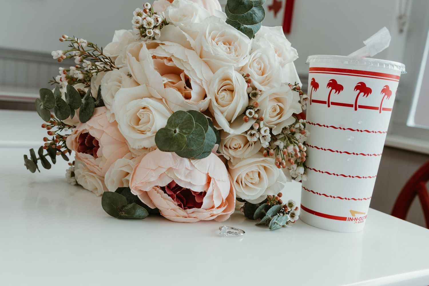 Wedding still life with peach roses and In-N-Out cup on white surface.