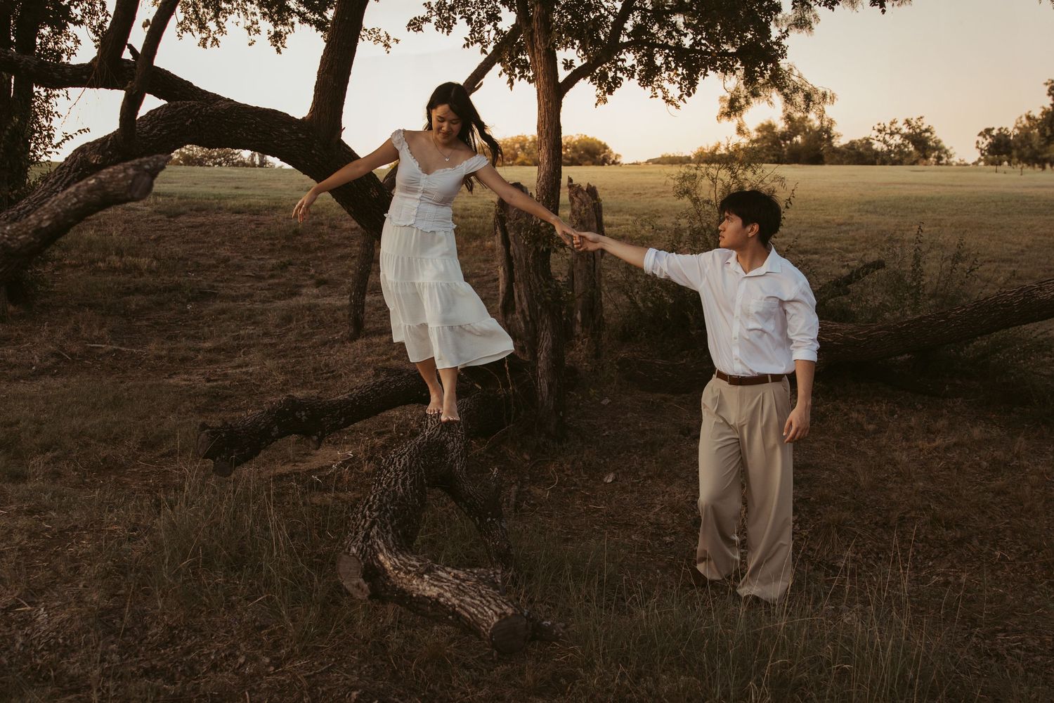A couple enjoys a romantic sunset moment on a hilltop with oak trees in the warm evening light.