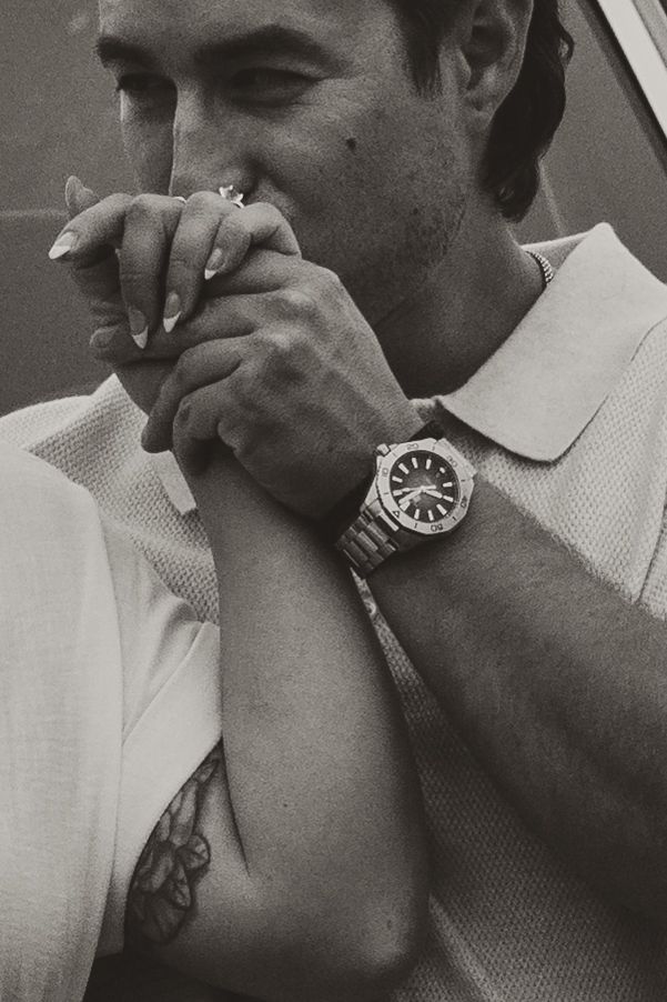 Black and white photo showing a person wearing a white polo shirt and luxury watch taking a drag from a cigarette.
