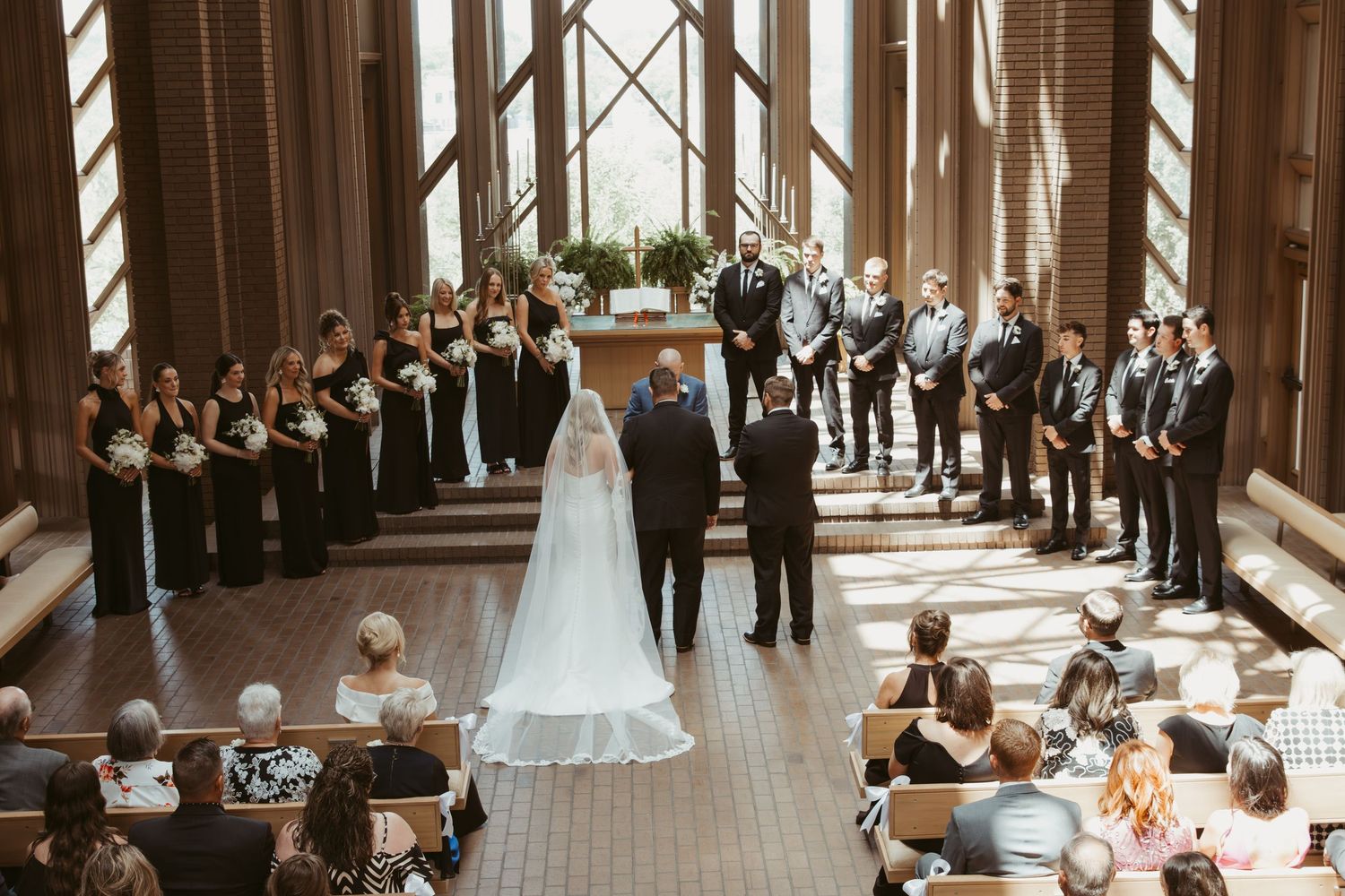 Wedding ceremony takes place in elegant indoor venue with wooden beams and natural lighting streaming through windows. Wedding Photographer