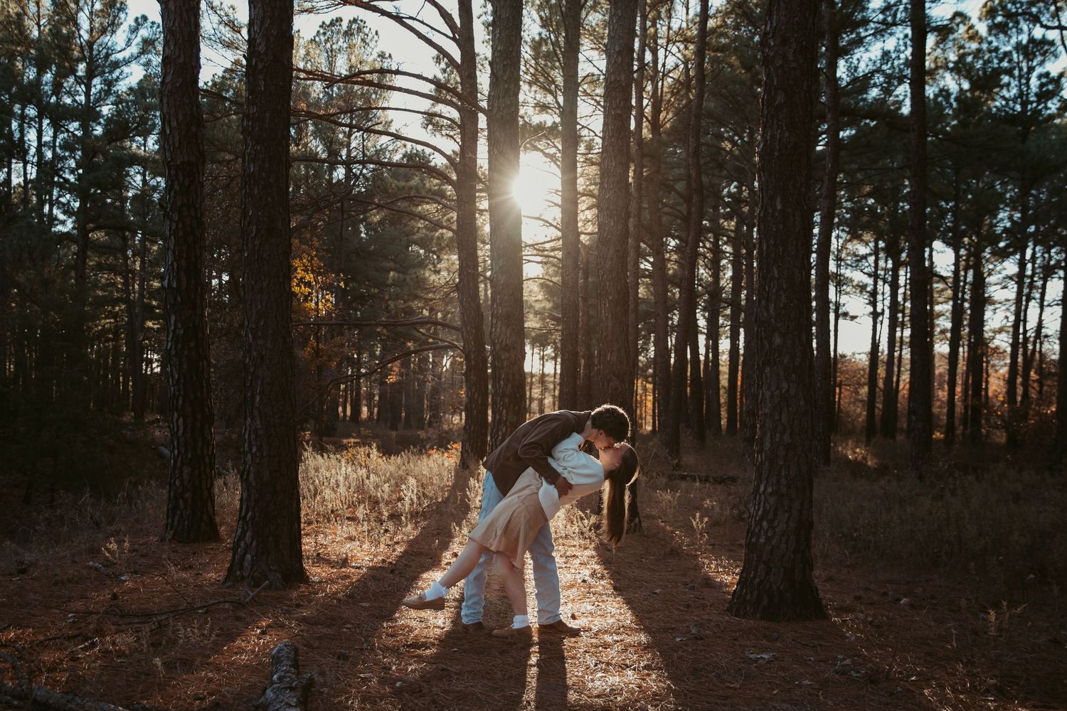 Silhouetted figures embrace in a romantic pose on a sunlit forest path during golden hour. engagement photos Fort Worth