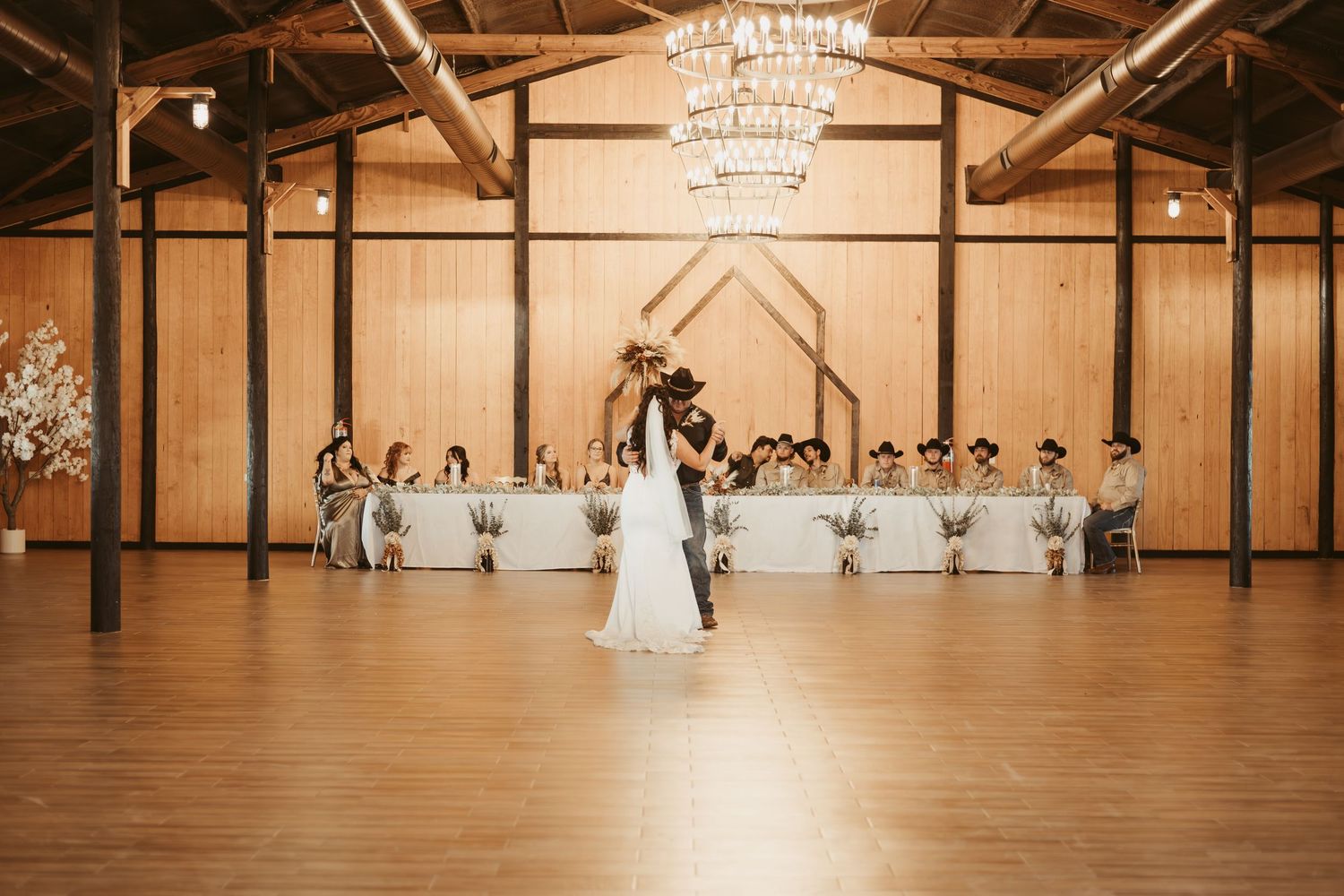 Wedding party arranged in symmetrical formation inside rustic wooden barn venue with chandeliers. Wedding photographer DFW