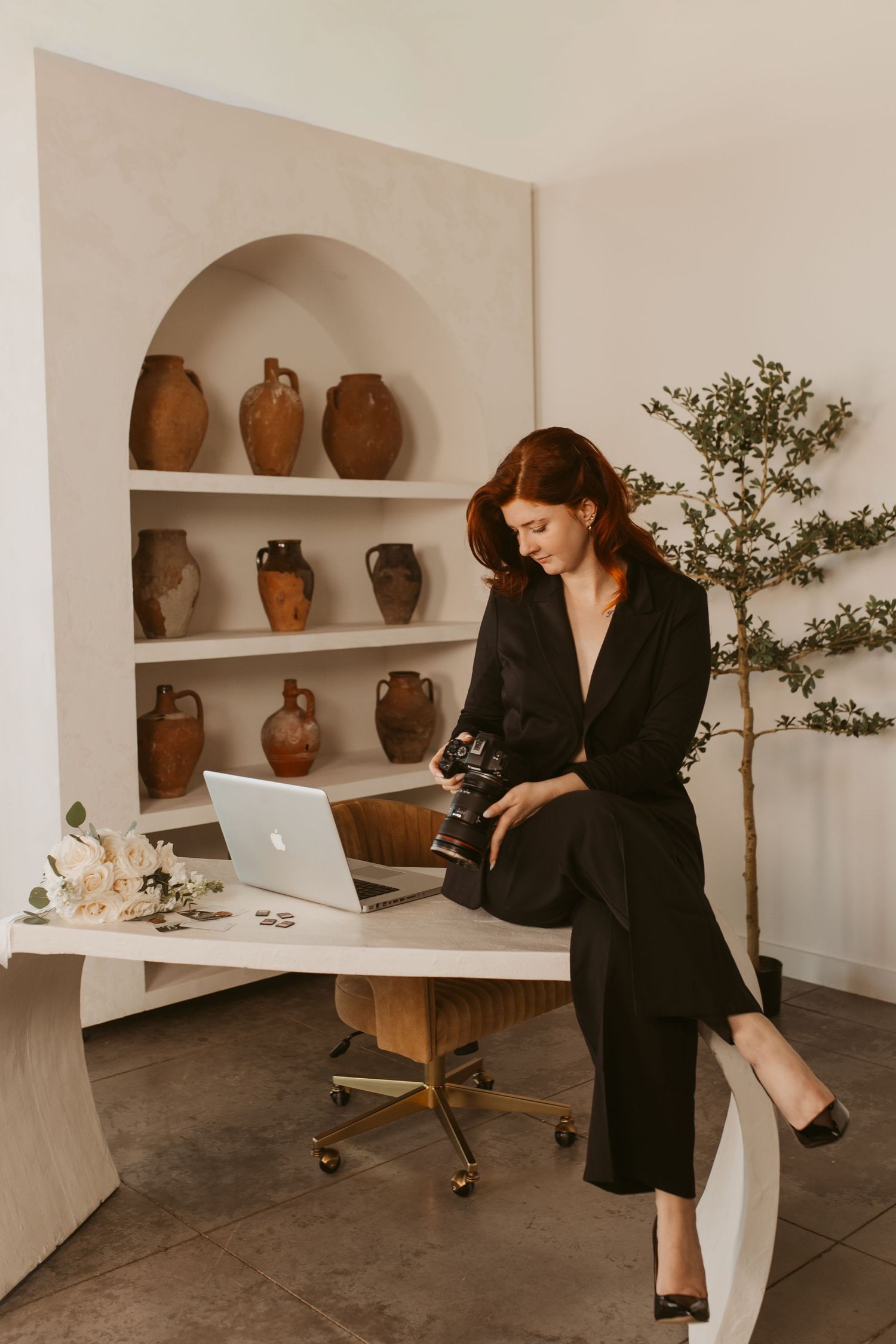 A minimalist workspace with clay pottery on white shelves features someone in black working at a desk.