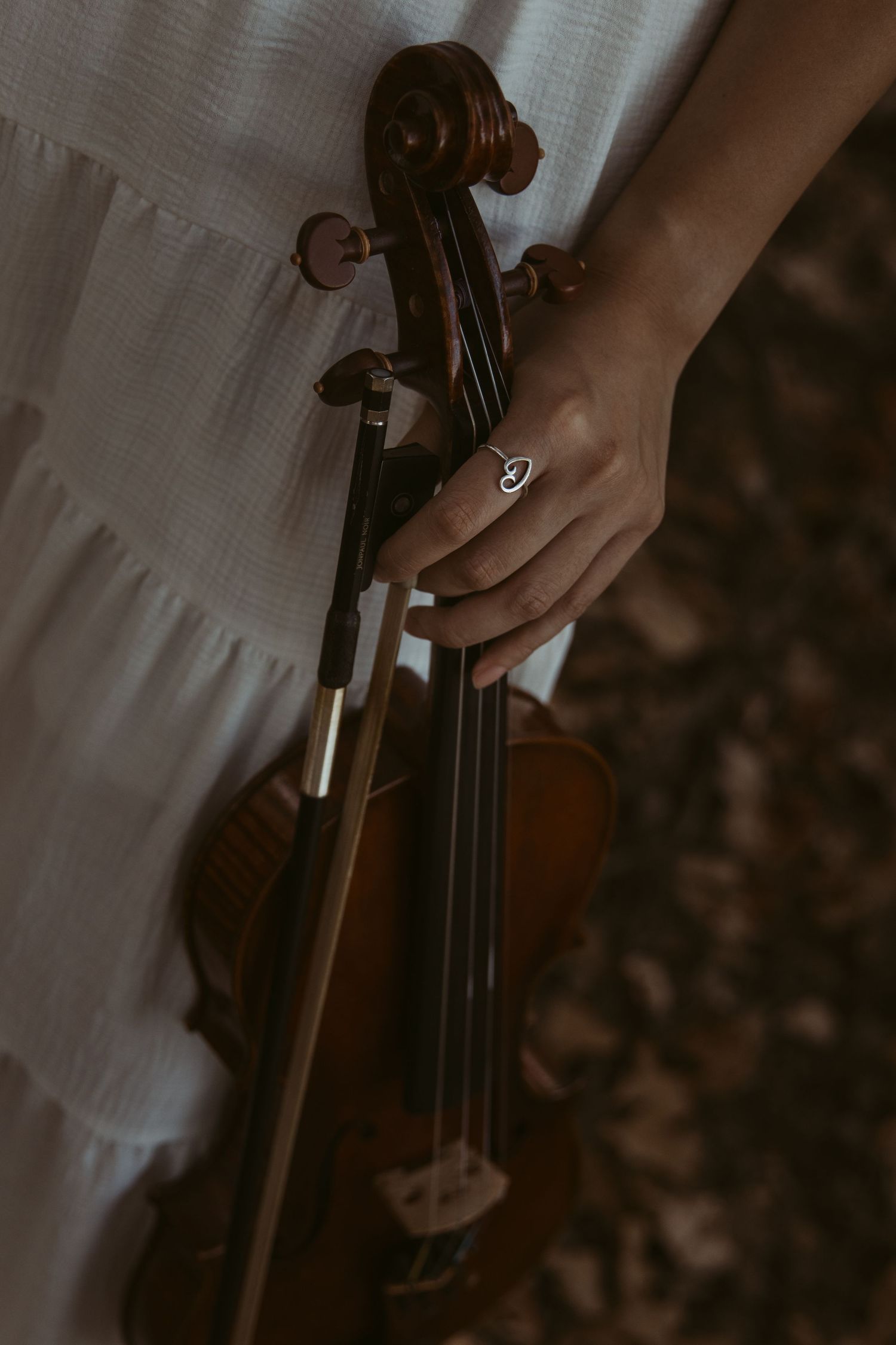 A close-up shot of a hand with a ring holding the neck of a violin against a light fabric background.