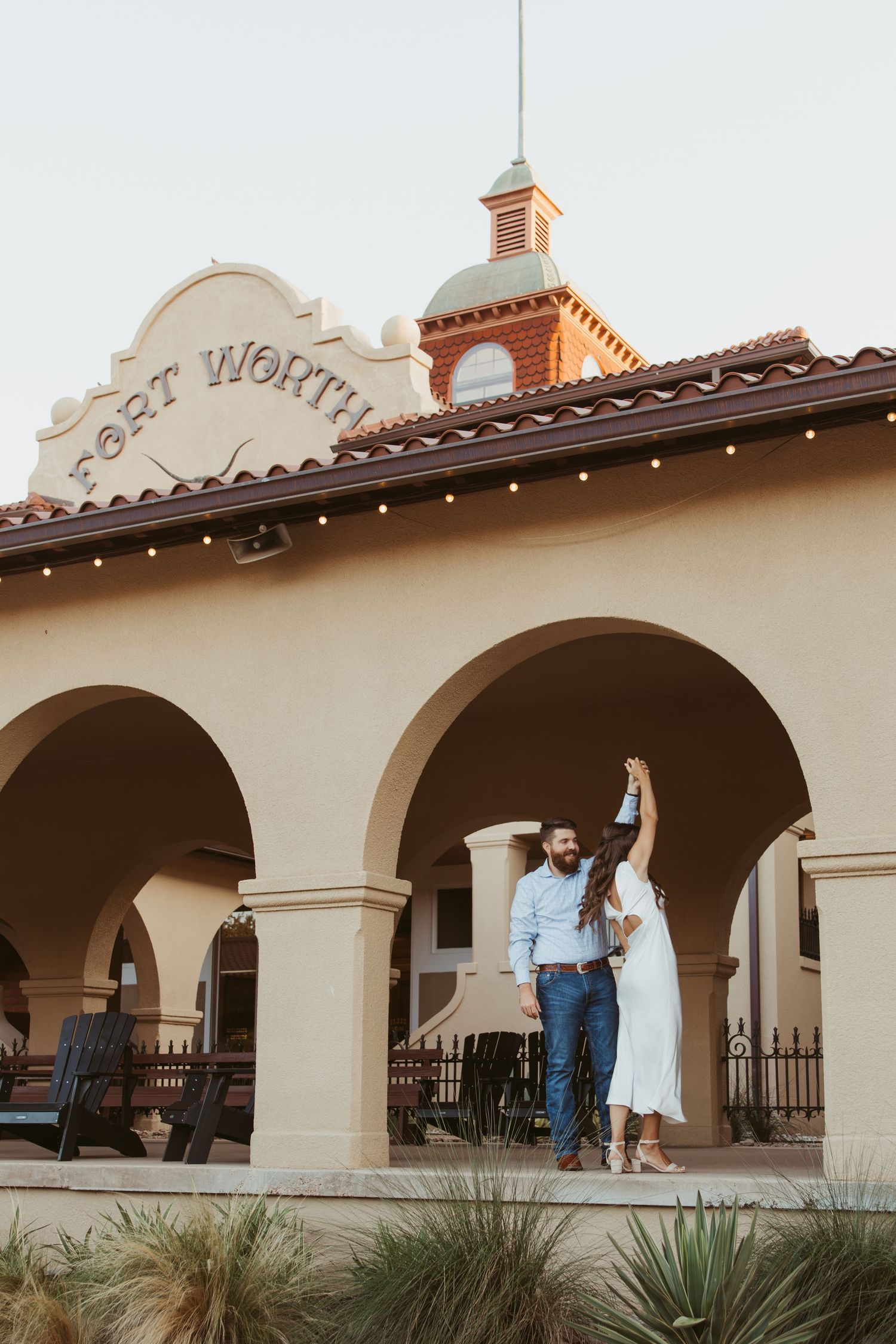Couple celebrates at historic Post Worth building with Spanish colonial architecture and arched entryway at sunset.