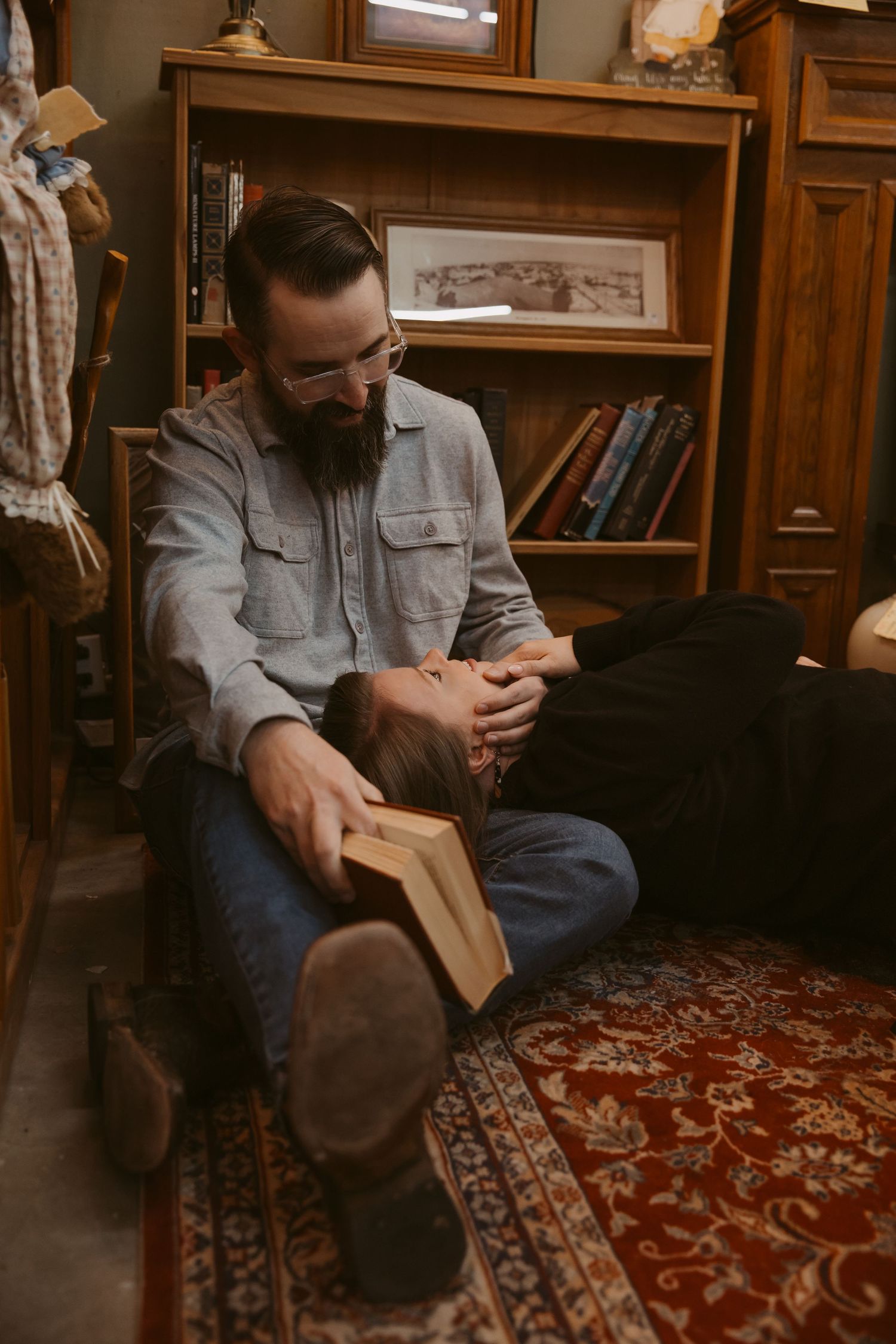 A person in casual attire sits on a patterned oriental rug while reading in a cozy library setting.