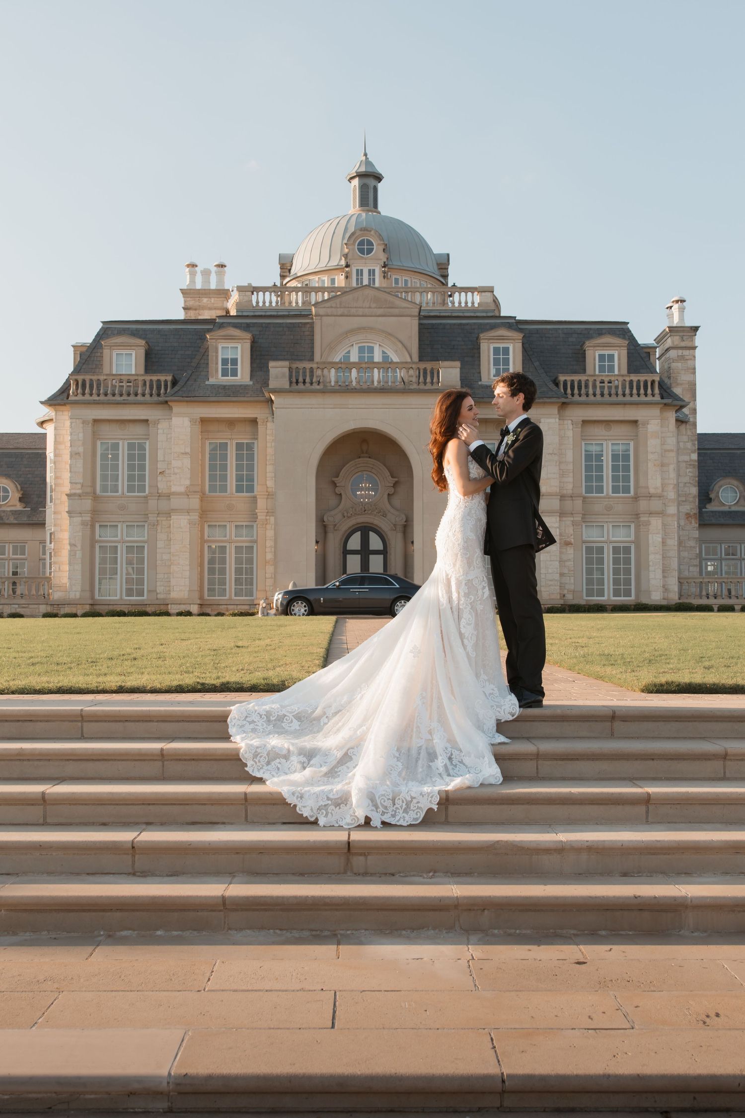 Newlyweds pose together in front of a grand French-style mansion with domed architecture.