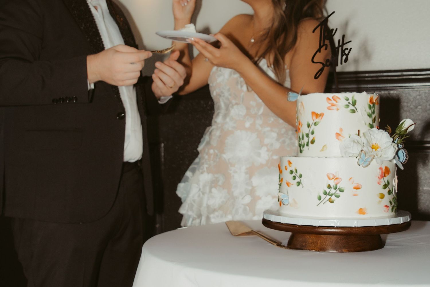 Wedding cake cutting moment with a white tiered cake decorated with colorful floral details.