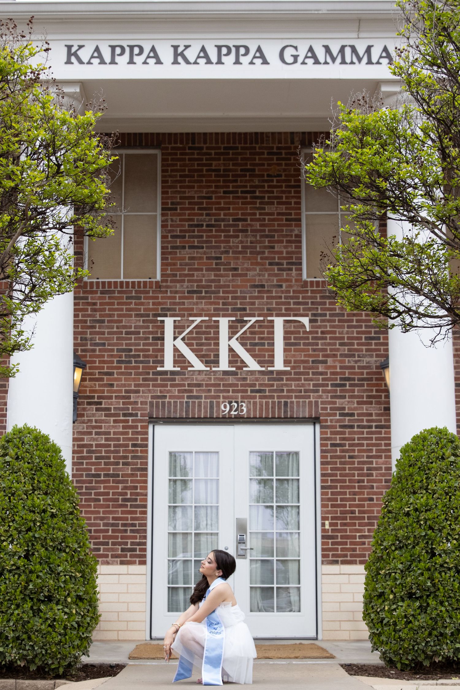 A person sits outside the brick entrance of the Kappa Kappa Gamma sorority house with white columns and Greek letters.