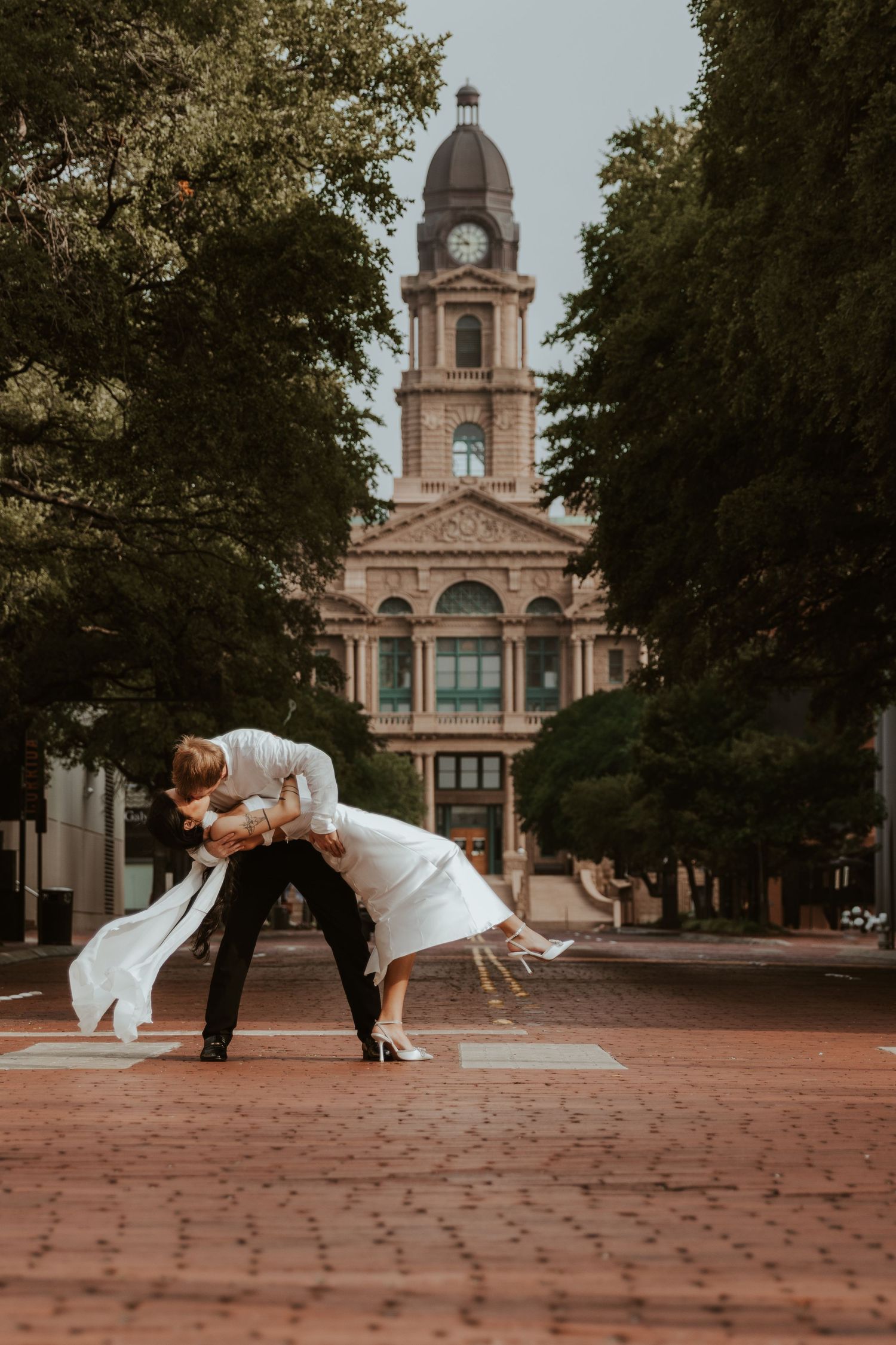 A romantic dance pose in front of a grand historic building with a copper dome and brick facade. Wedding Photographer DFW