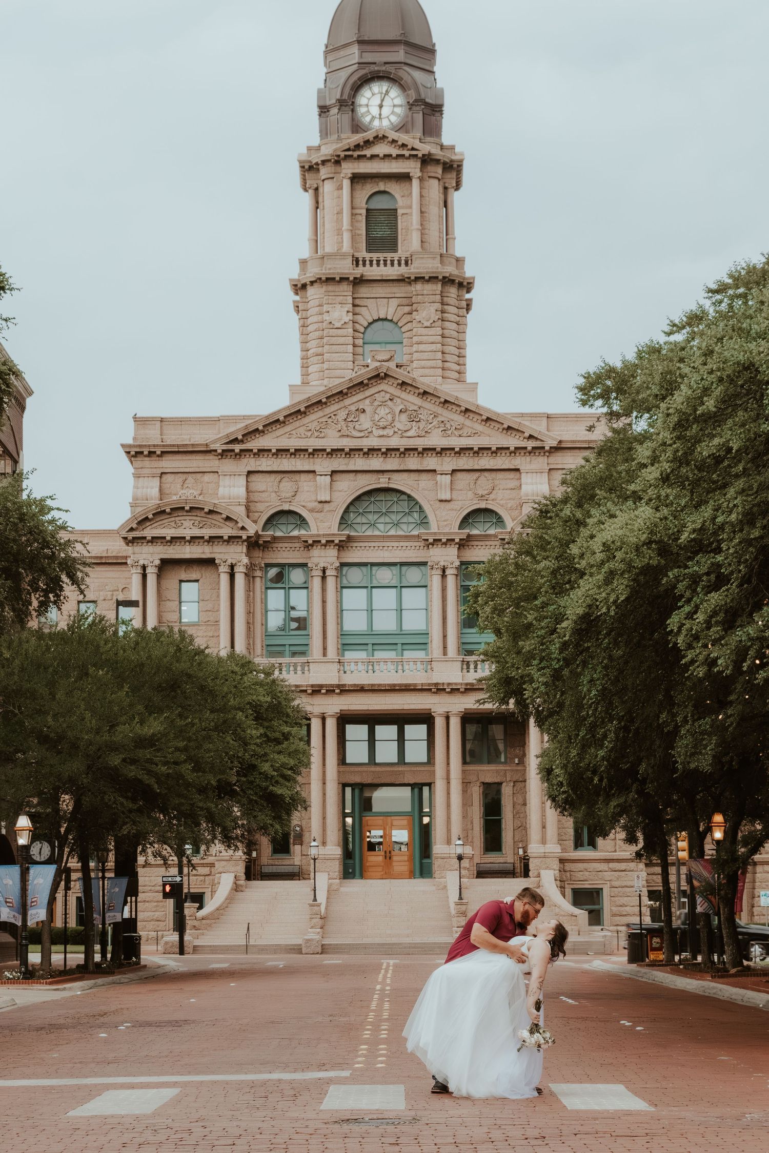 A romantic wedding moment in front of a grand historic courthouse with clock tower.