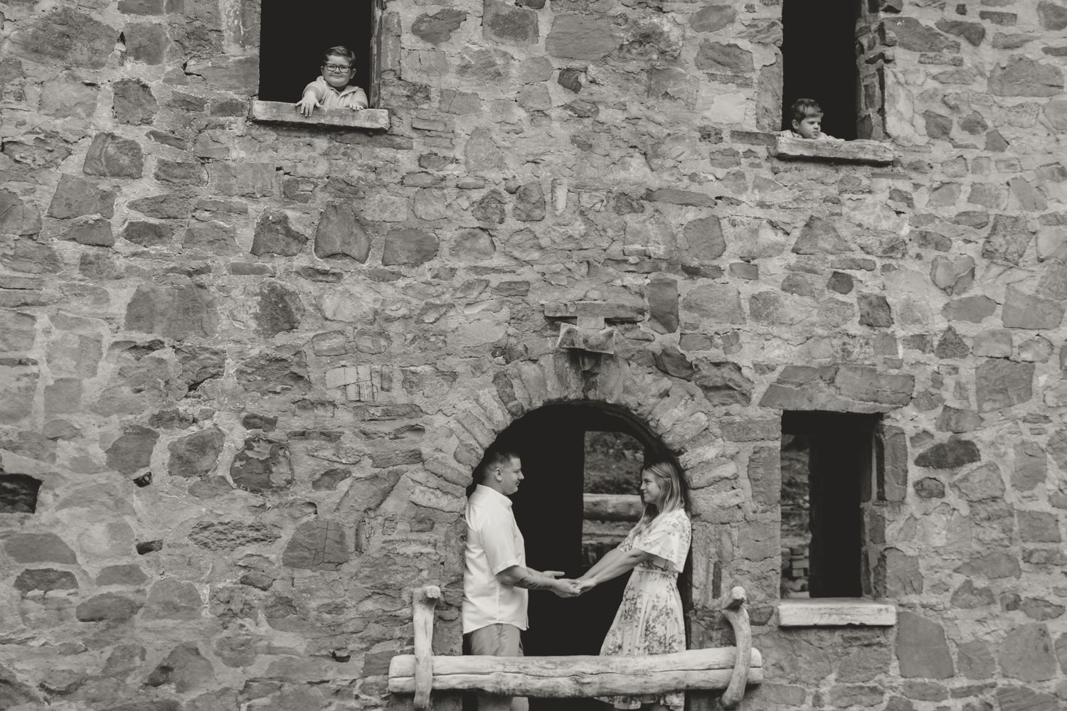 A black and white image of two people standing at a window in an old stone building.