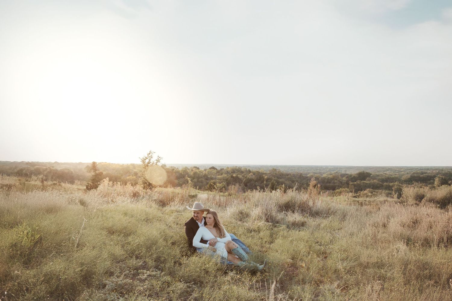 Couple embraces in tall grass field during golden sunset.