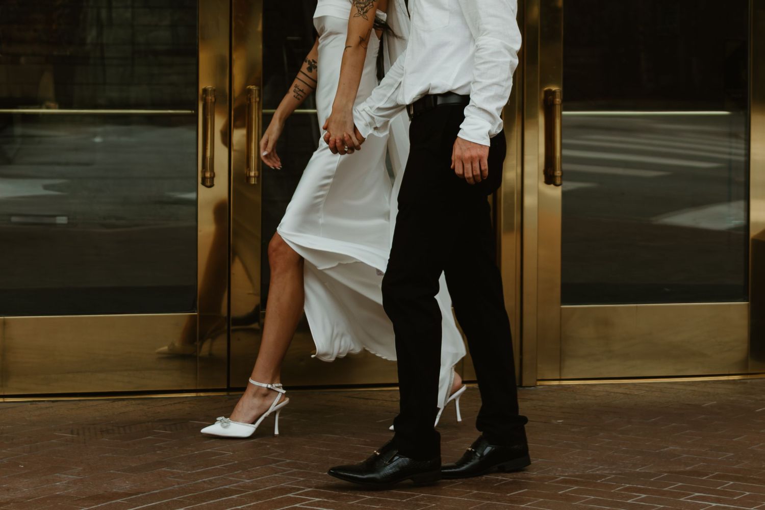 Two people in formal attire walking together, showing only their legs and feet against a dark background. Engagement photographer DFW